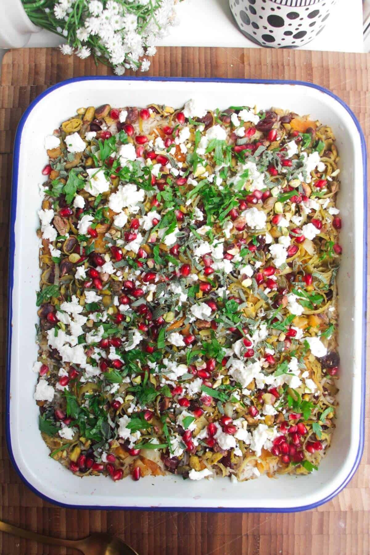 Baked rice topped with feta, pomegranate seeds and herbs in an oven dish.