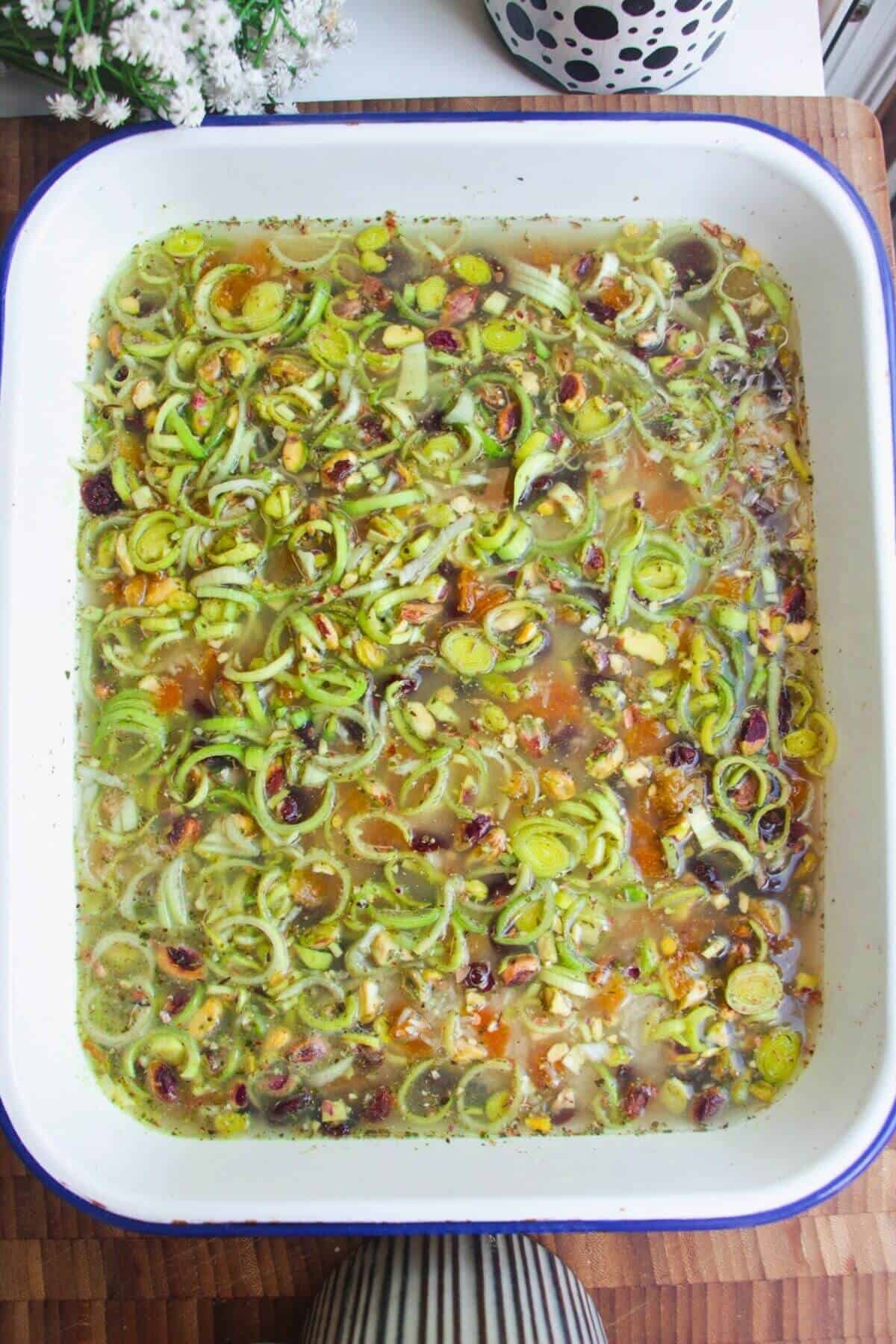Rice, leeks, seasoning and stock in a large white oven dish.