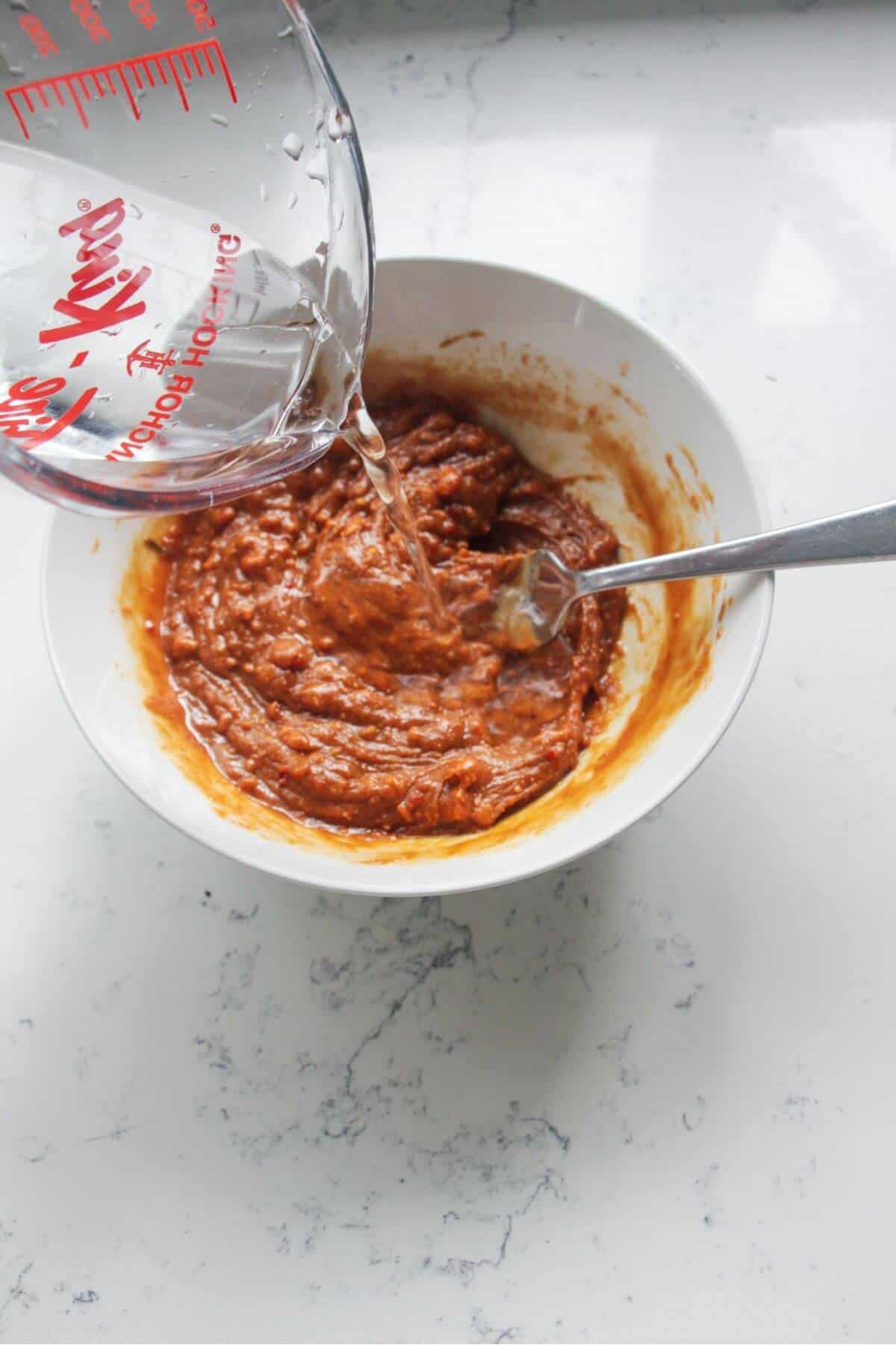 Pouring water into peanut sauce in a small bowl.
