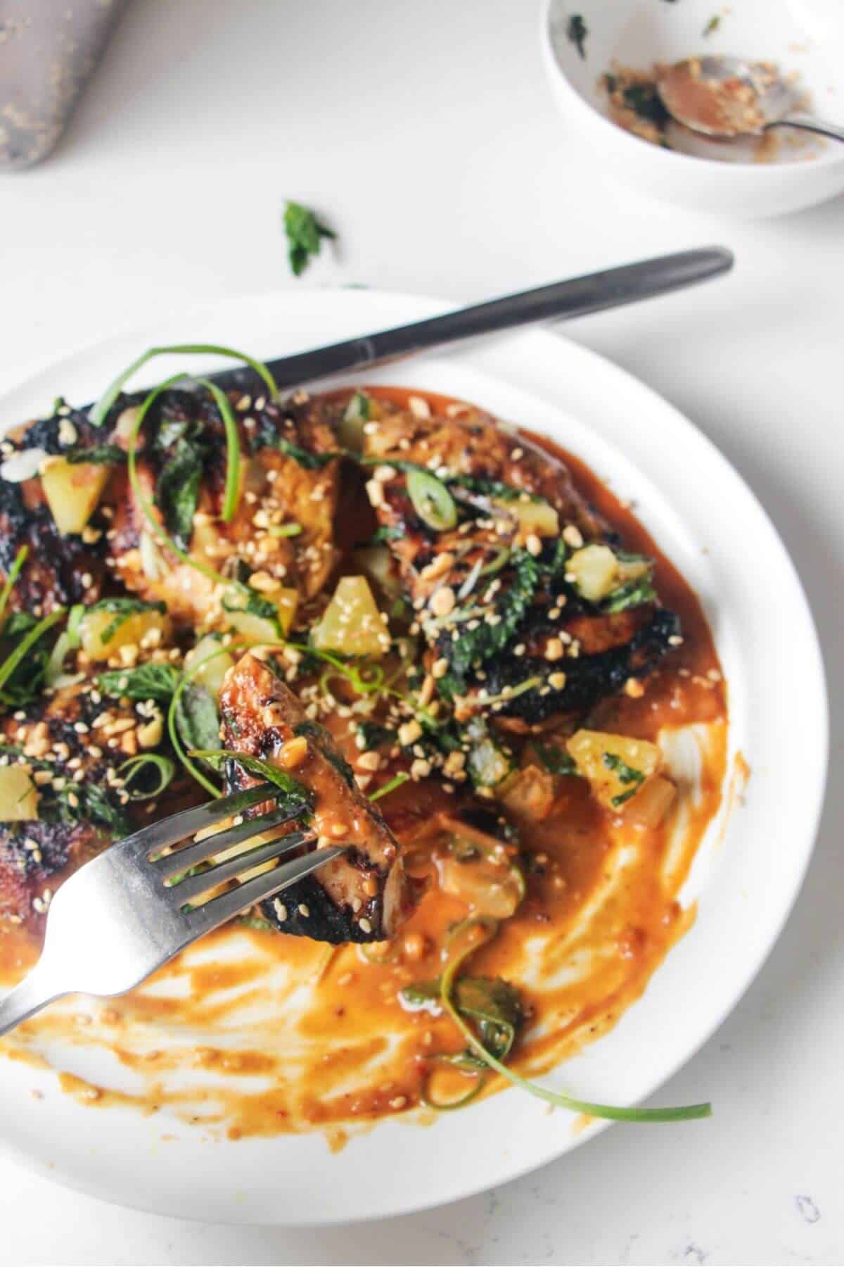Charred peanut chicken on a spoon, with peanut sauce on the plate.
