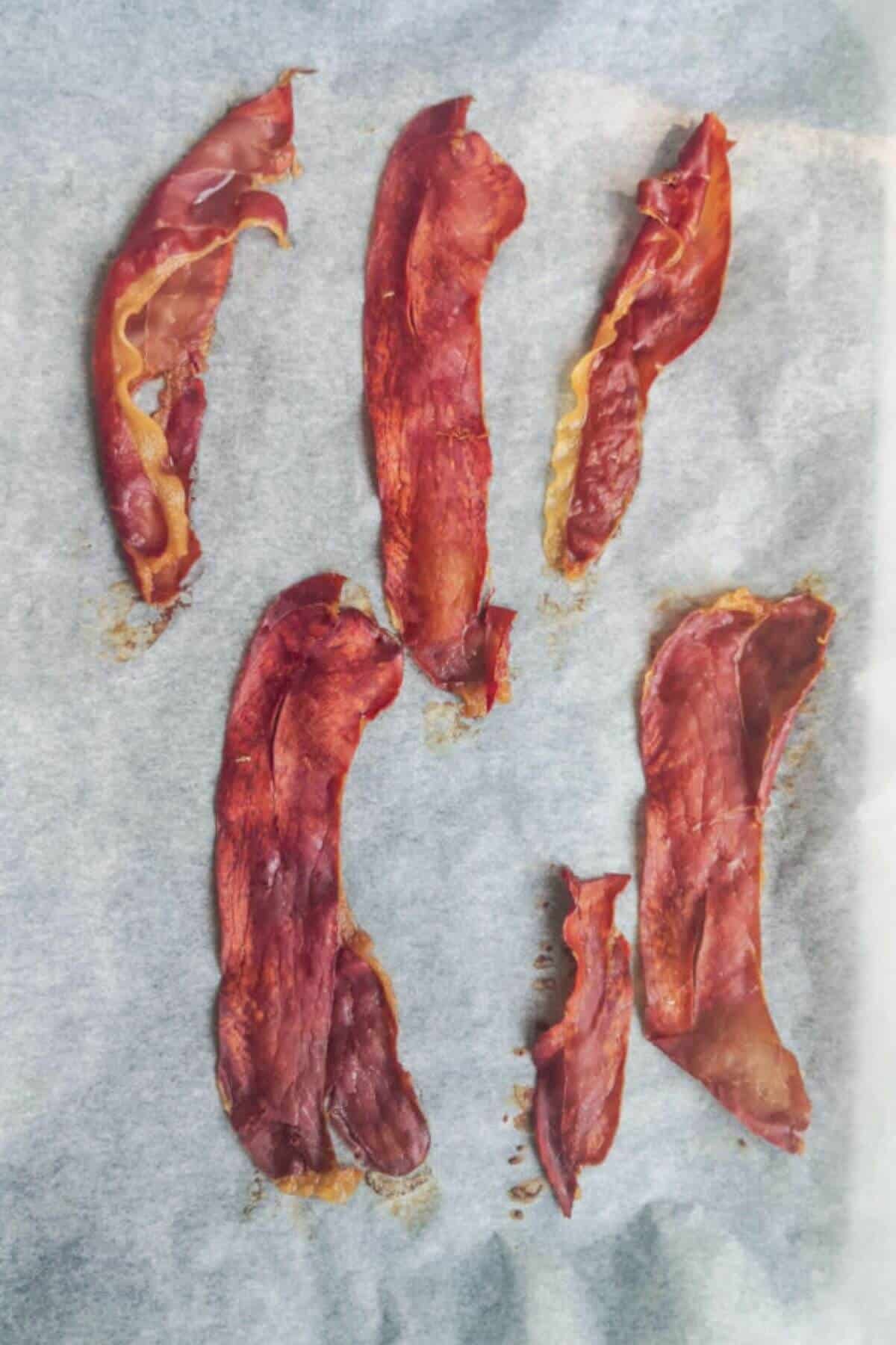 6 strips of crispy prosciutto laid out on a baking paper lined oven tray.