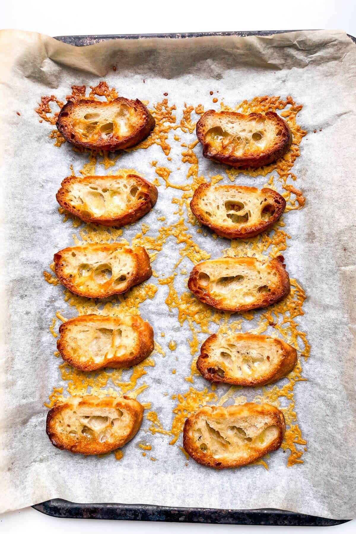 Crispy cheese with baguette slices on top on a lined baking tray.