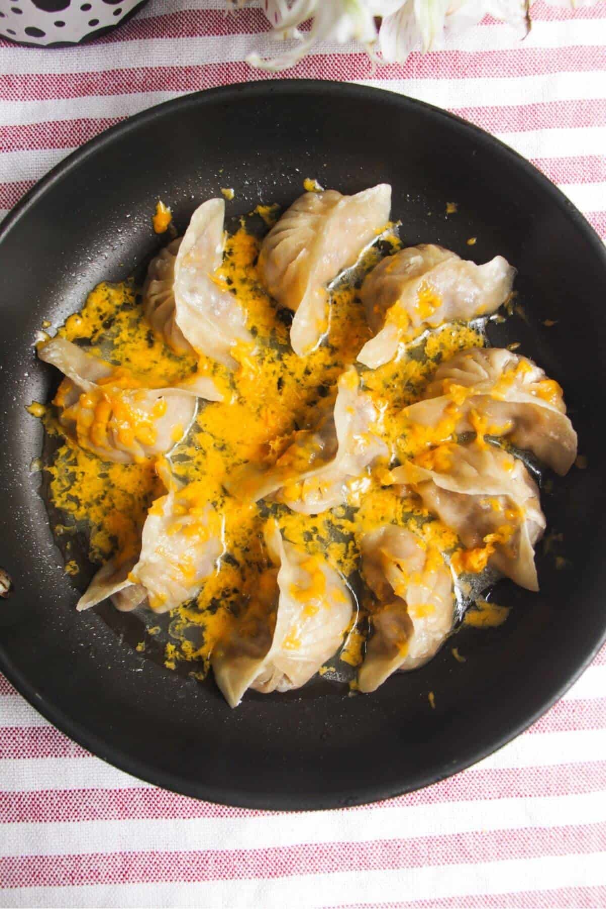 Grated cheese on top of cheeseburger dumplings in a small pan.