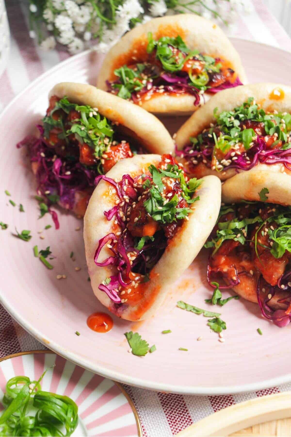 Five Korean chicken filled bao buns on a pink plate with aioli on the side.