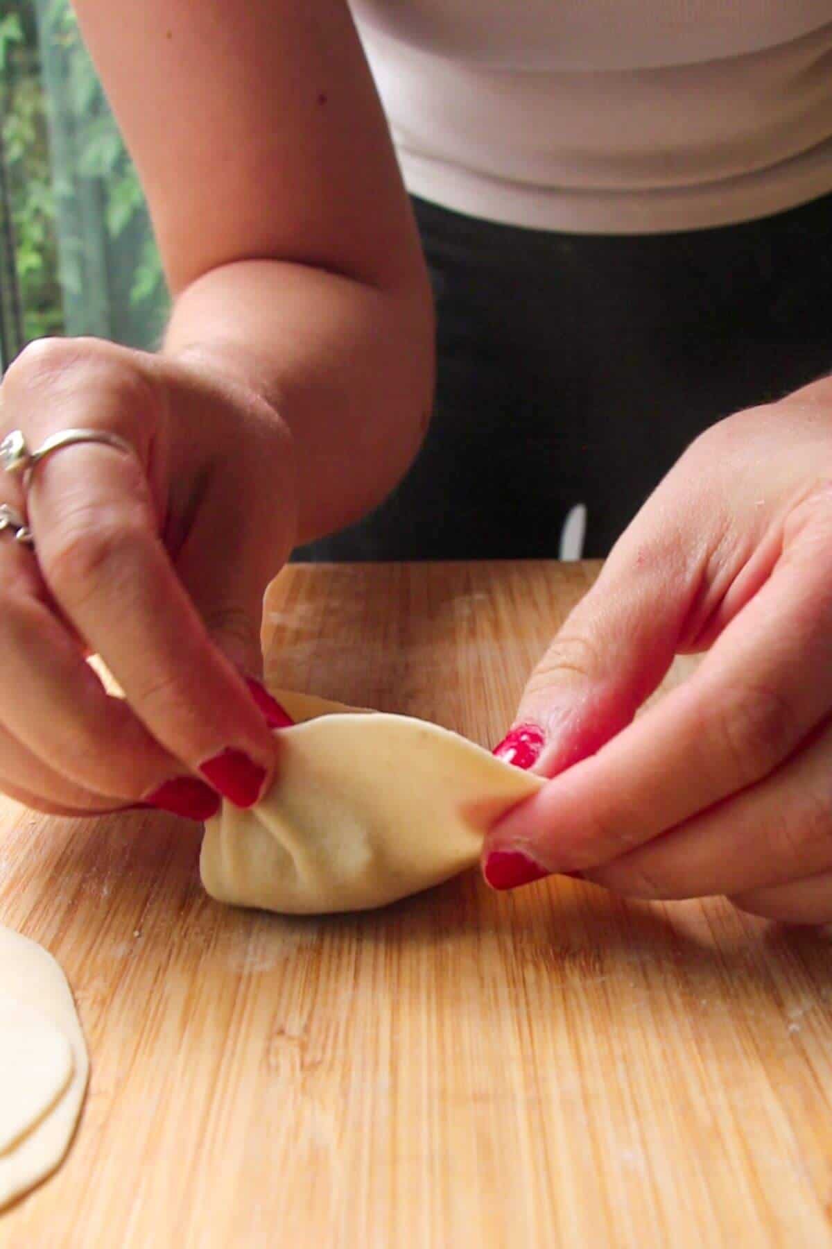 Hands folding dumpling on a wooden board.