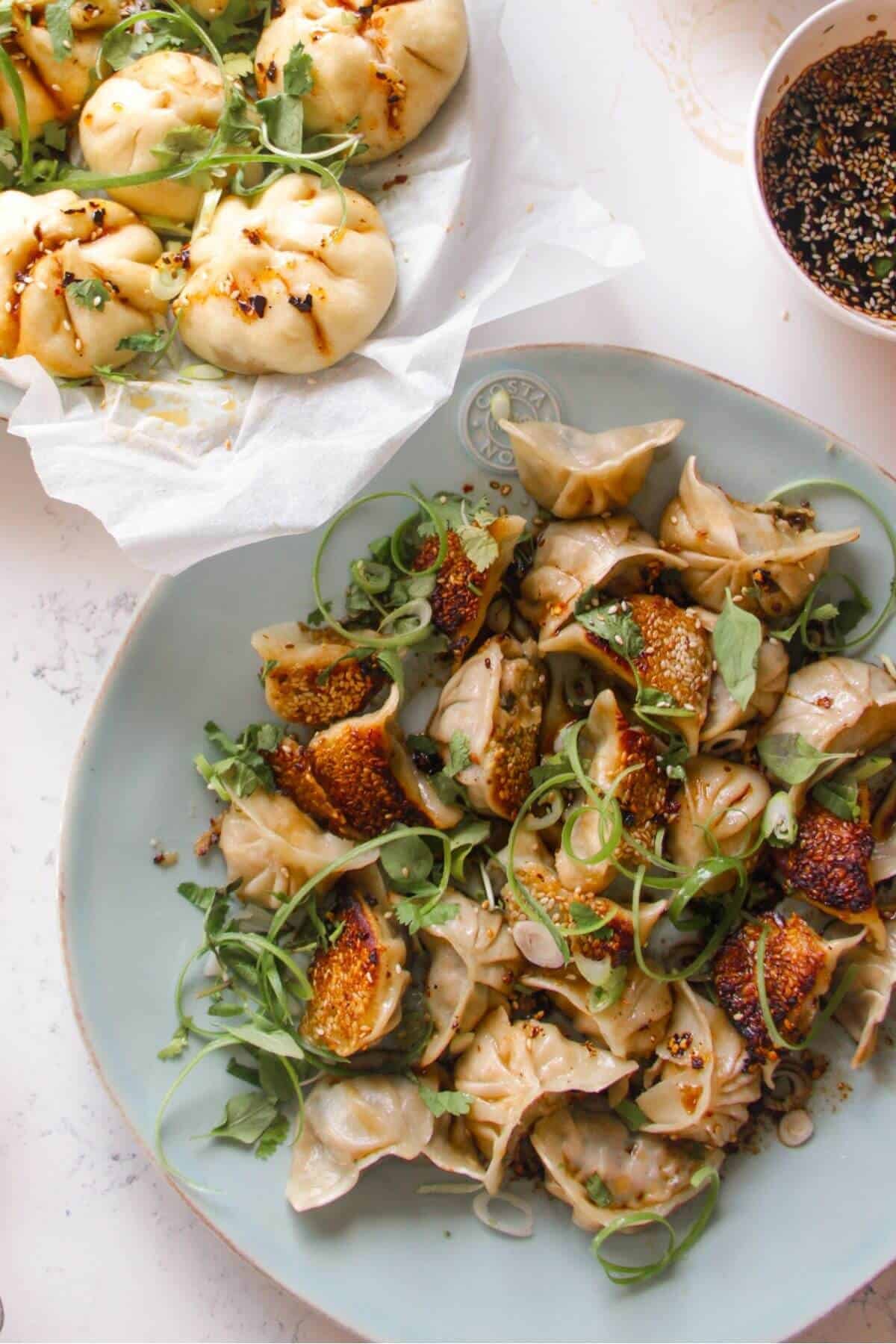 Chicken potstickers on a large blue plate with sauce and steamed buns on the side.