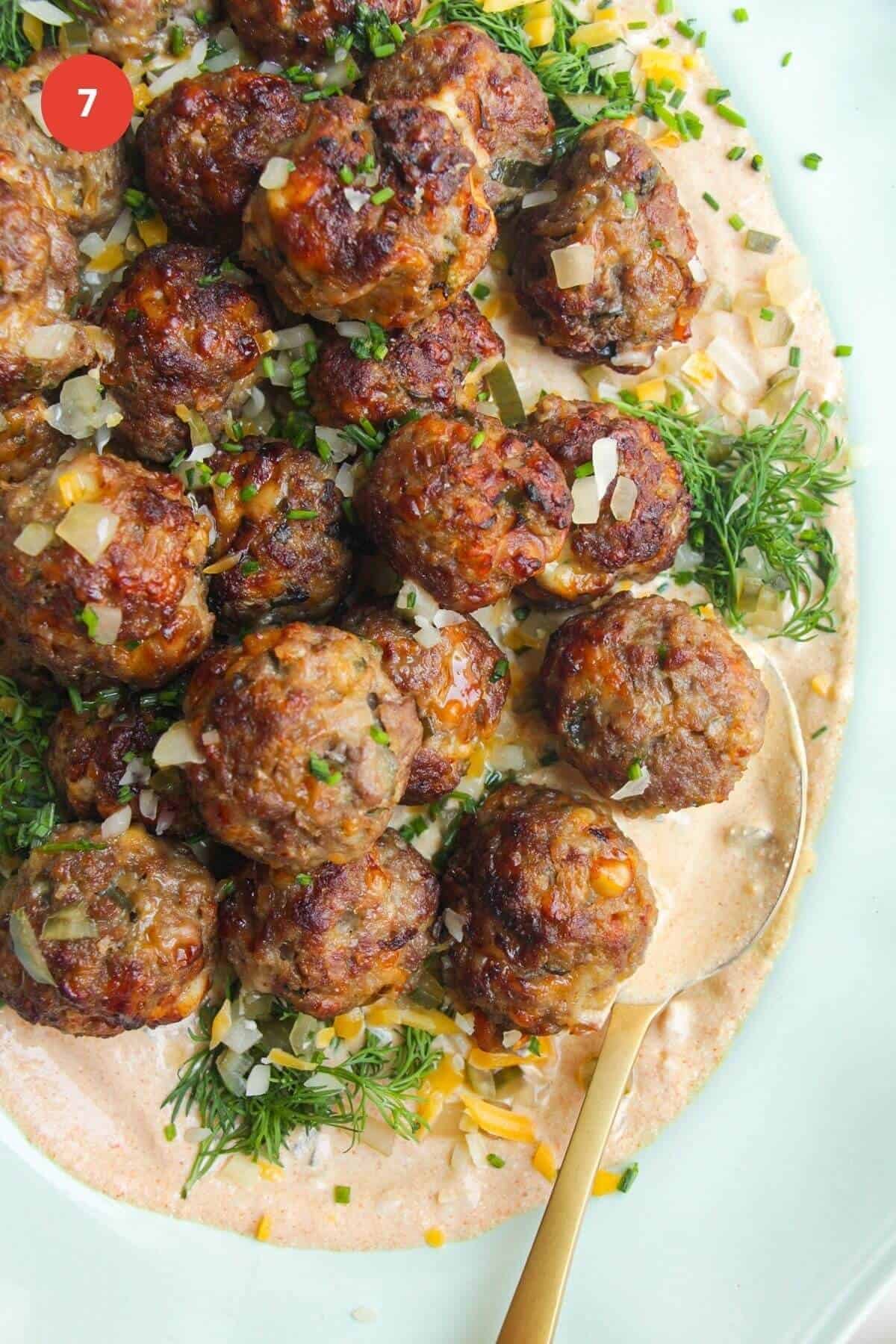 Cheeseburger meatballs on burger sauce on a platter.