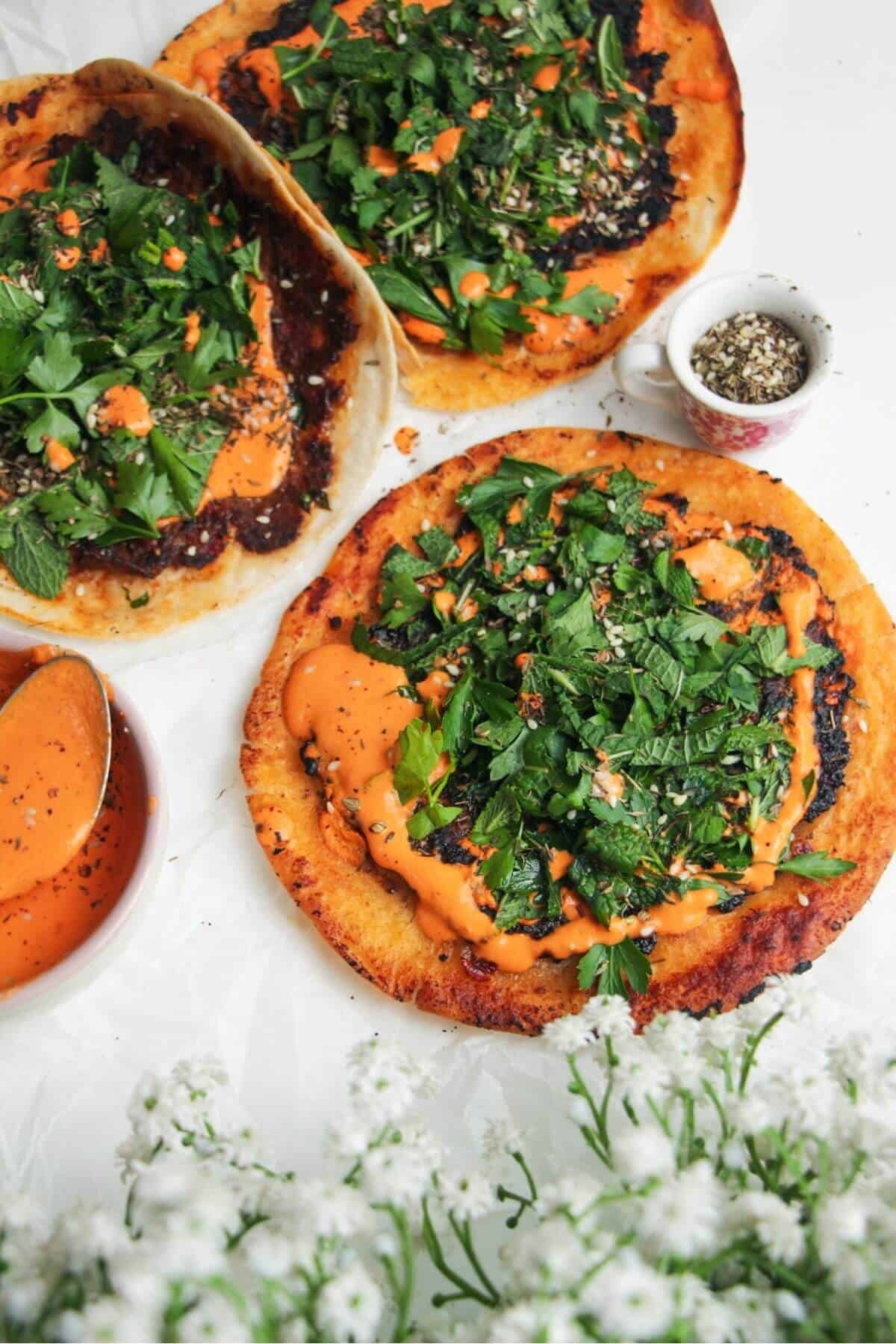 Smash lahmacun taco with red pepper sauce and herby salad on top.