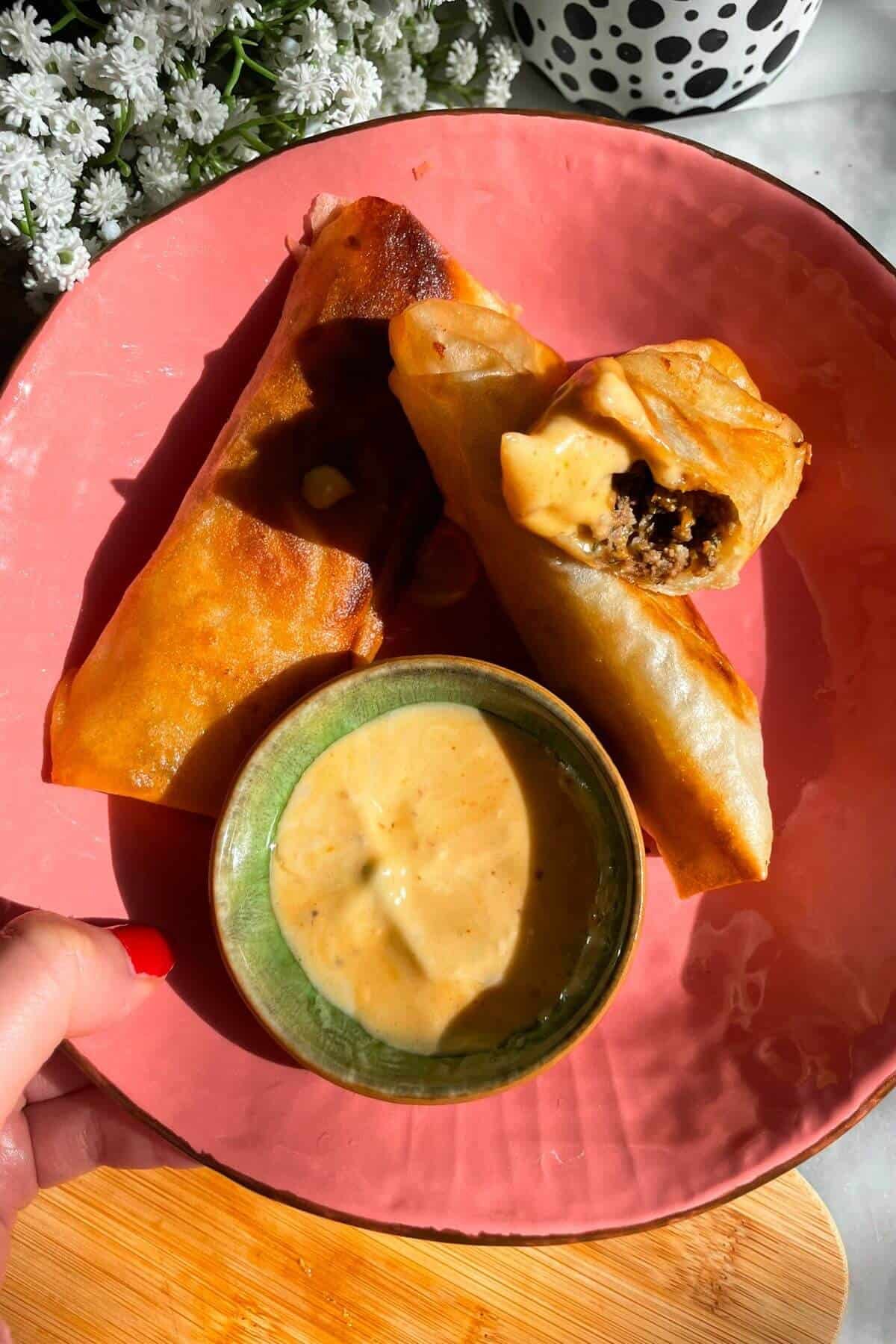Three cheeseburger spring rolls in a pink plate.
