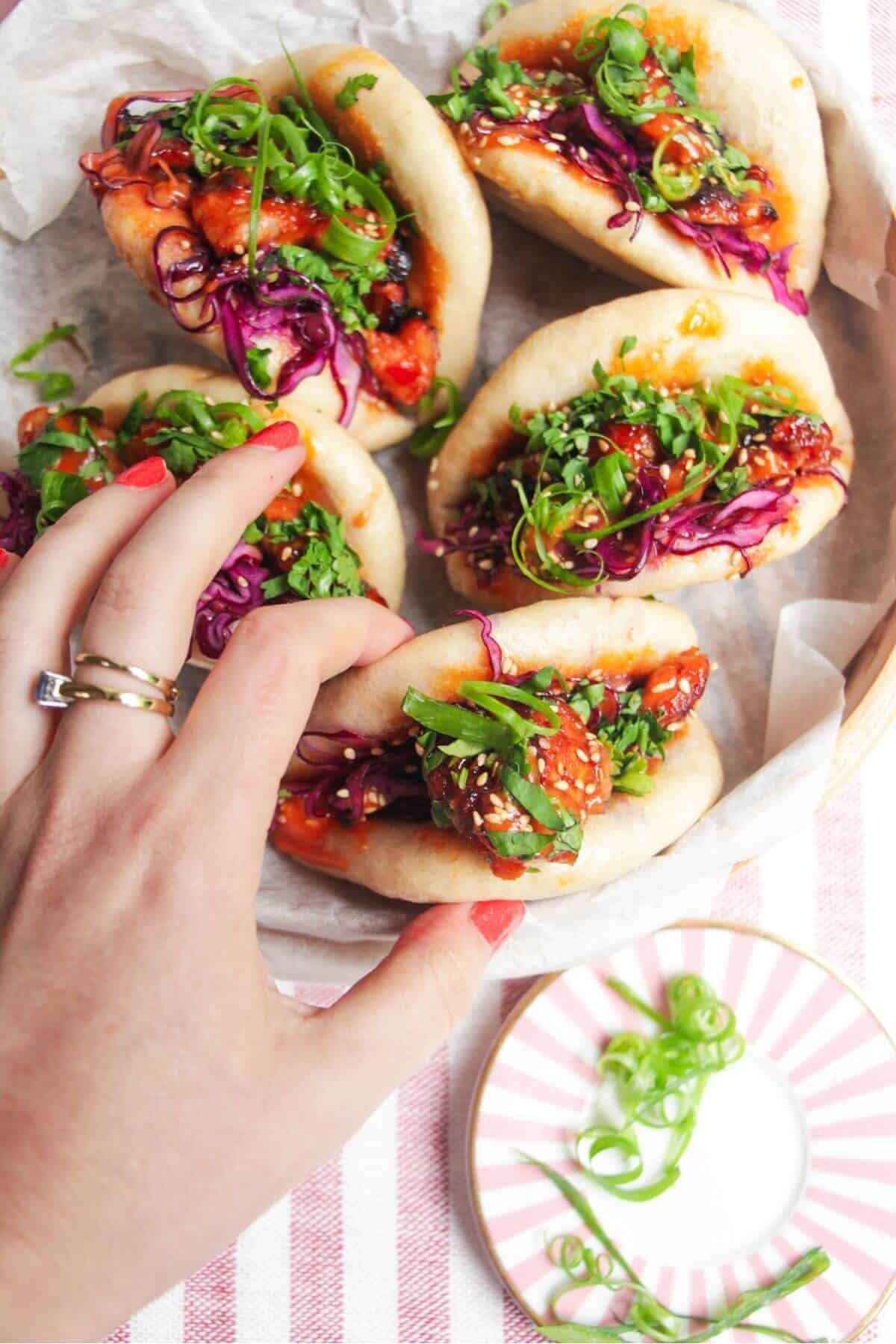 Five Korean chicken filled bao buns on a pink plate with aioli on the side.