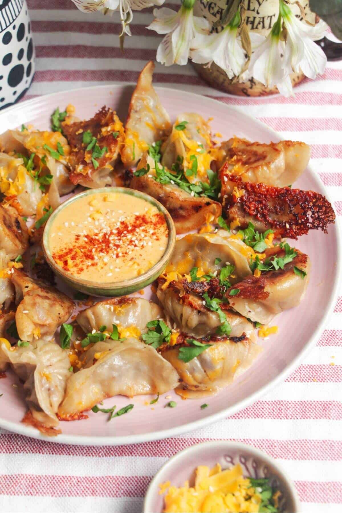 Crispy cheeseburger dumplings on a pink plate with small bowl of burger sauce in the middle.