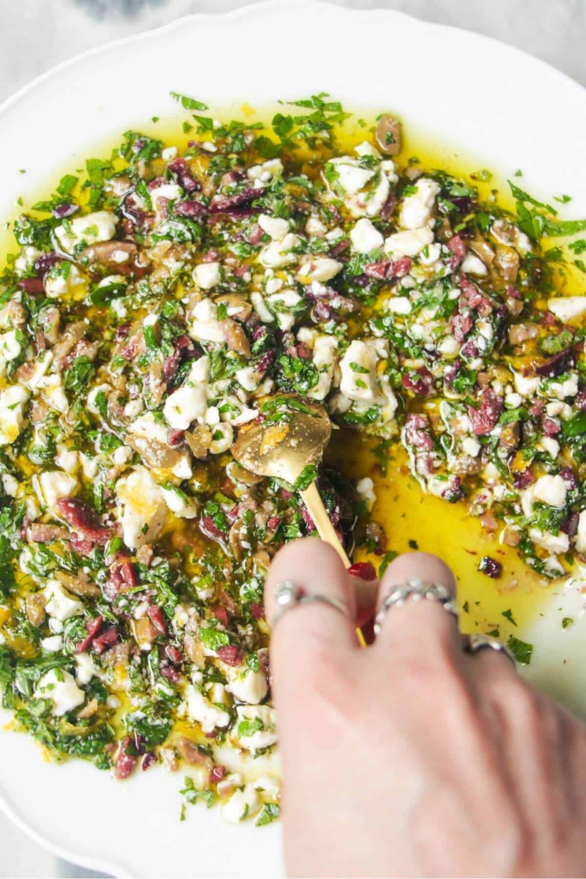 Hand mixing ingredients for Greek dipping oil in a large white plate.