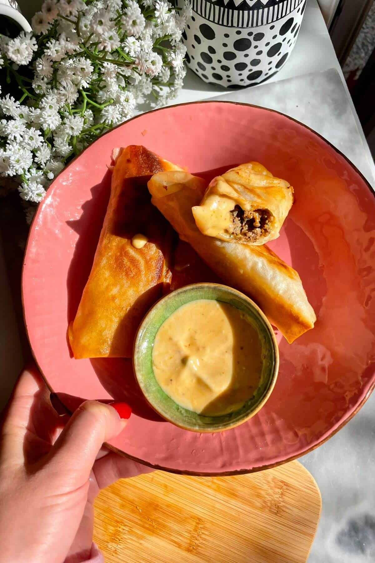Three cheeseburger spring rolls in a pink plate.