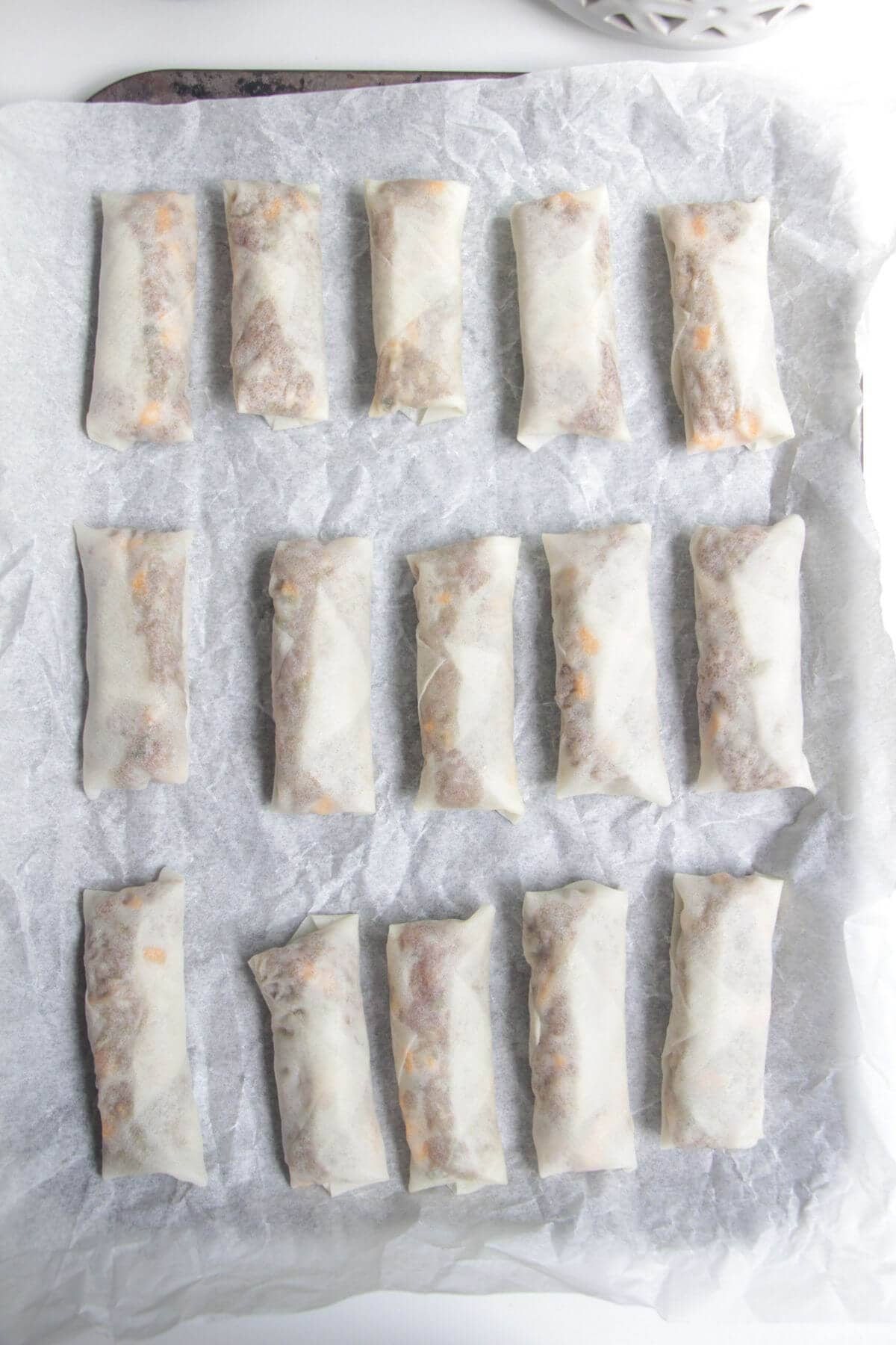 Cheeseburger spring rolls on a lined oven tray.