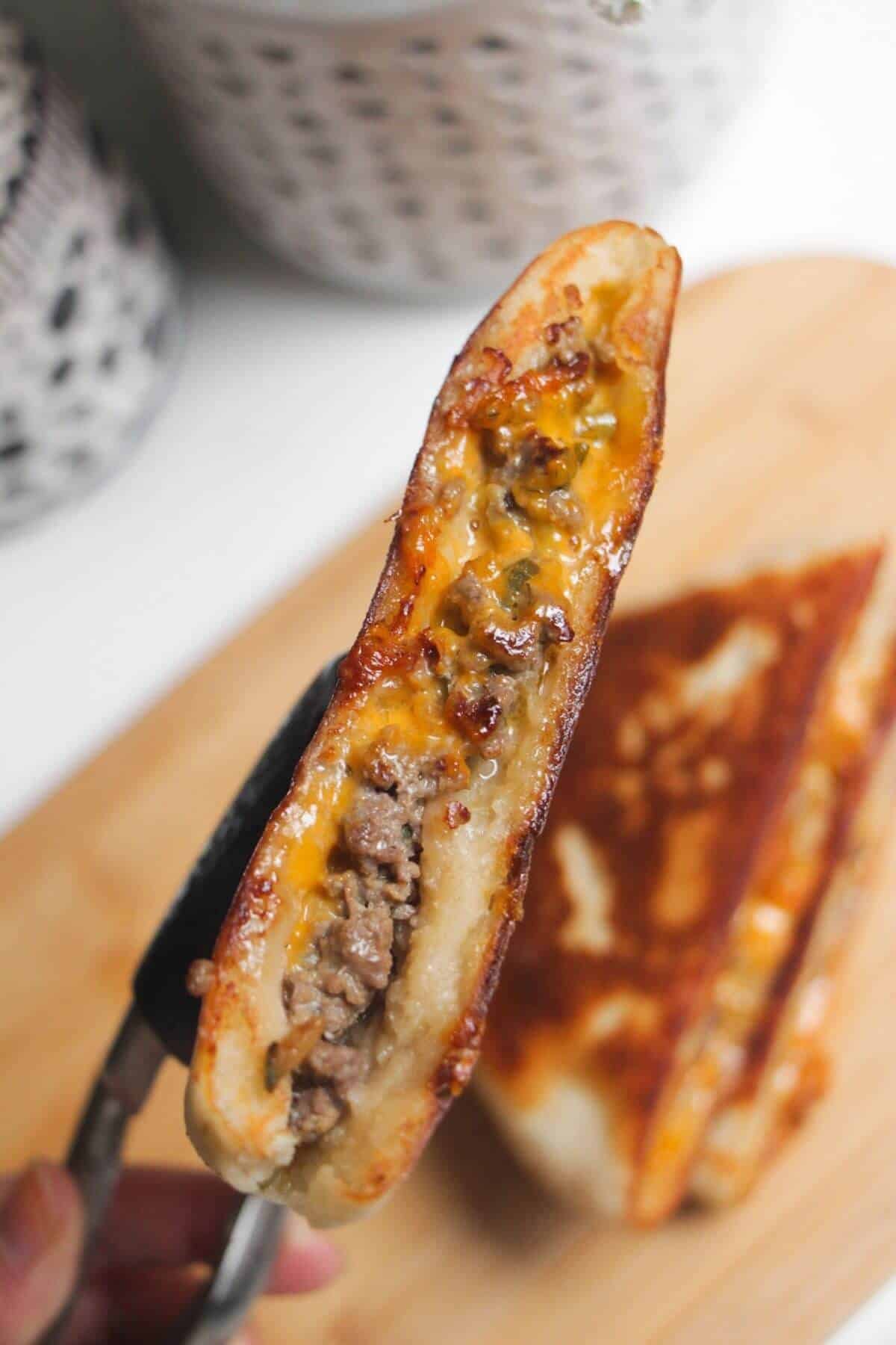 Tongs holding up cooked cheeseburger flatbread.