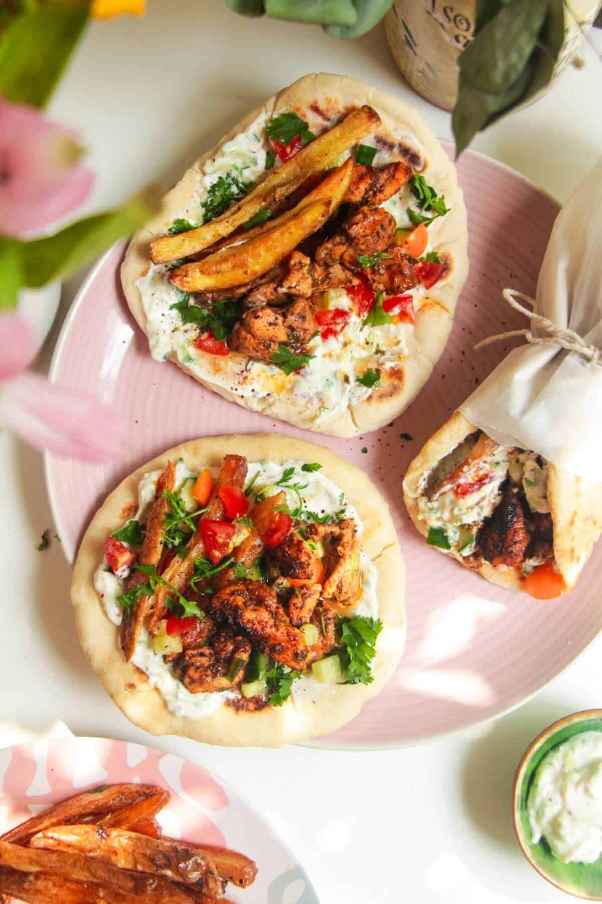 Three chicken gyros flatbreads on a pink plate.