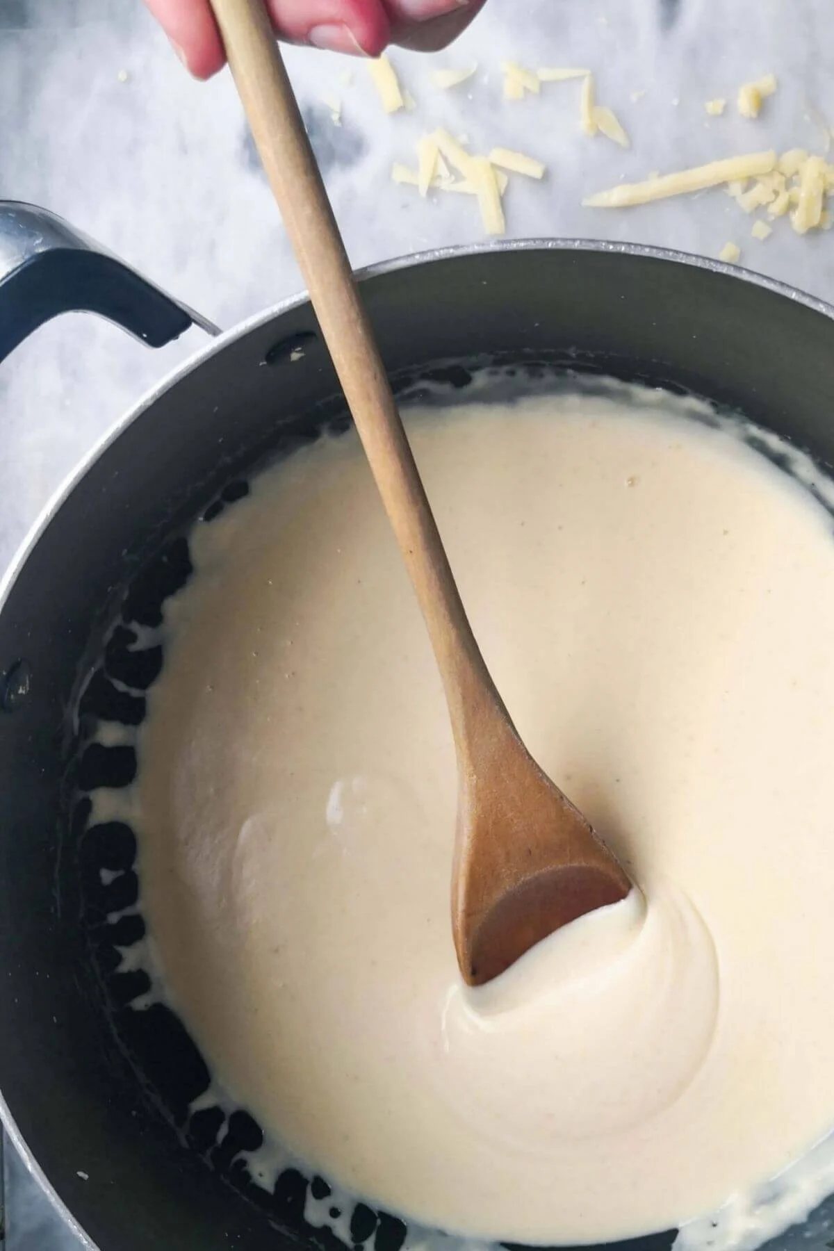 Cheesy bechamel sauce in a pot with a wooden spoon.