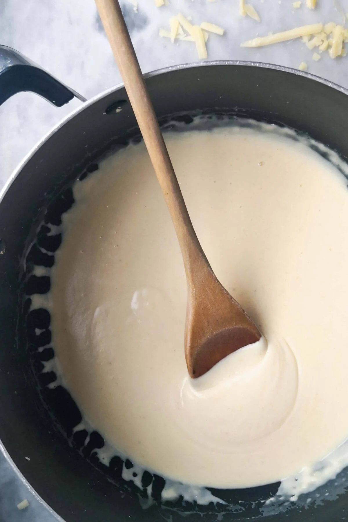 Cheesy bechamel sauce in a large black pan with a wooden spoon.