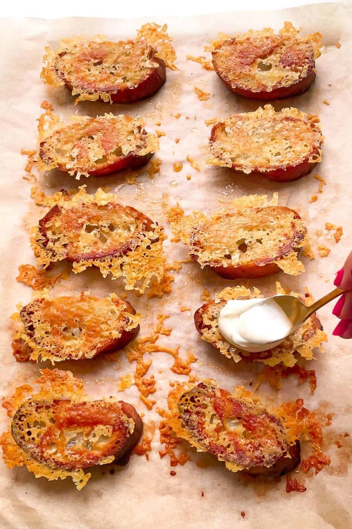 Spooning labneh on top of cheesy crostini on a lined tray.