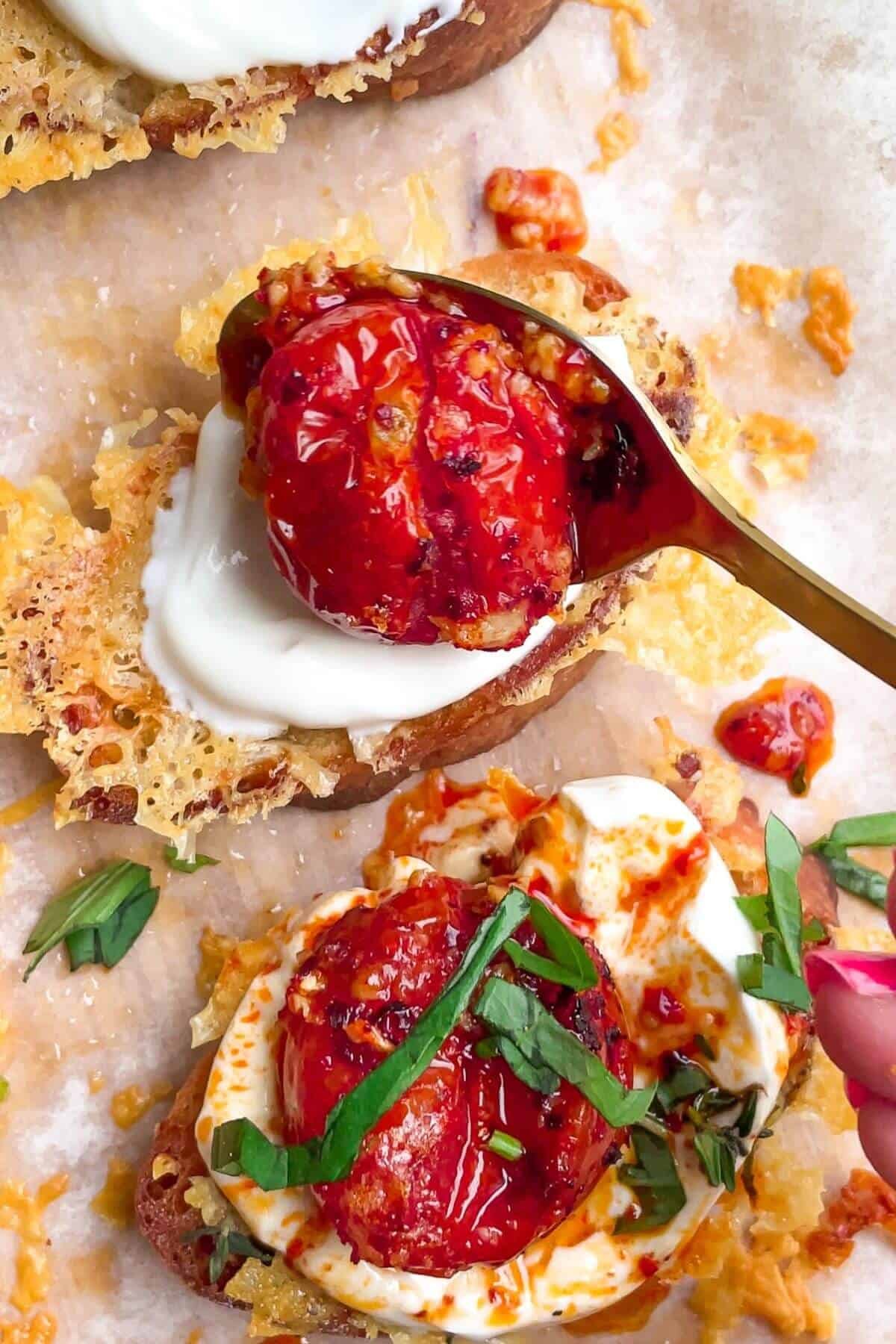 Spponing roasted cherry tomato onto labneh on top of cheesy crostini.