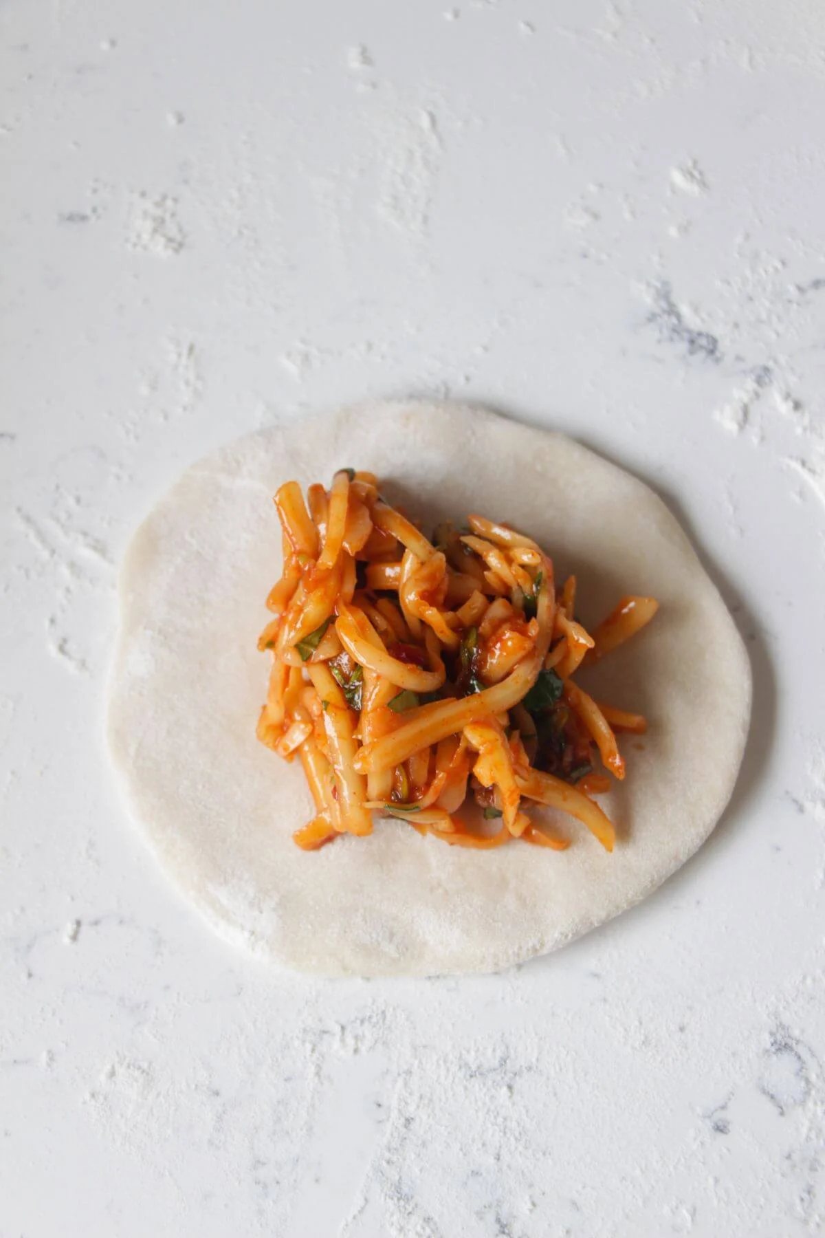 Cheesy gochujang mix piled onto a round circle of dough on a white marble background.