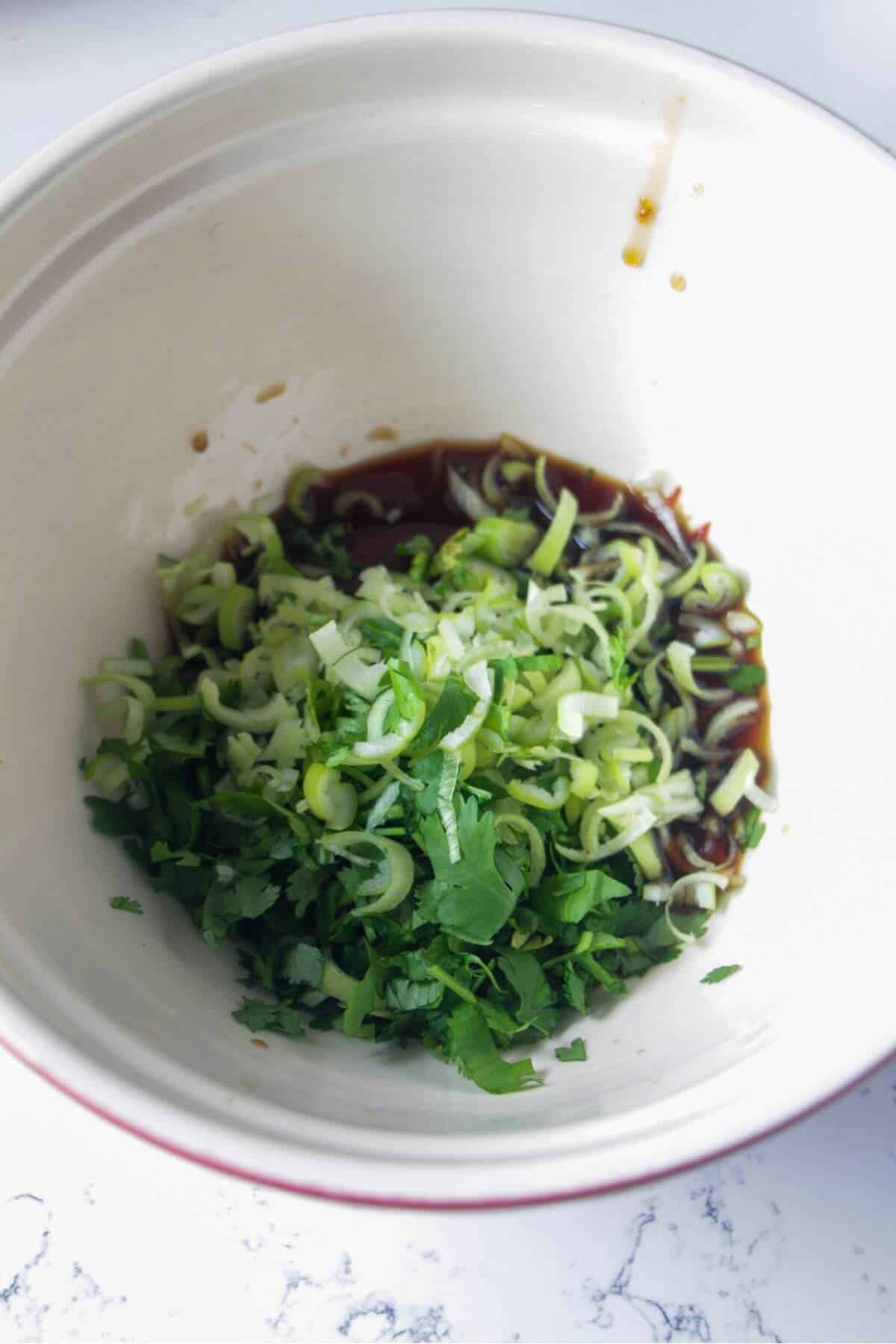 Scallions, cilantro, gochujang paste, soy sauce and chilli jam in a large white bowl.