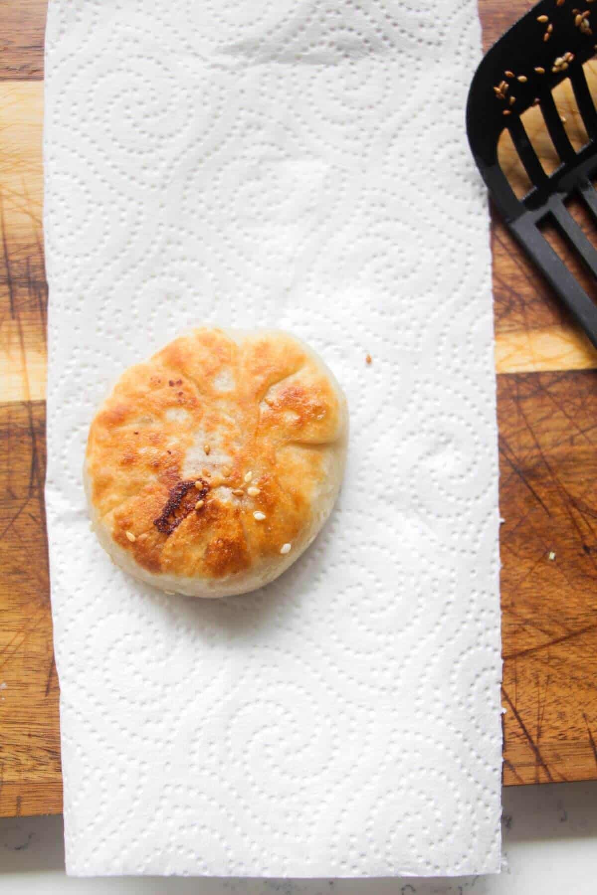 Pan-fried pizza pocket on a piece of kitchen towel on a wooden board.