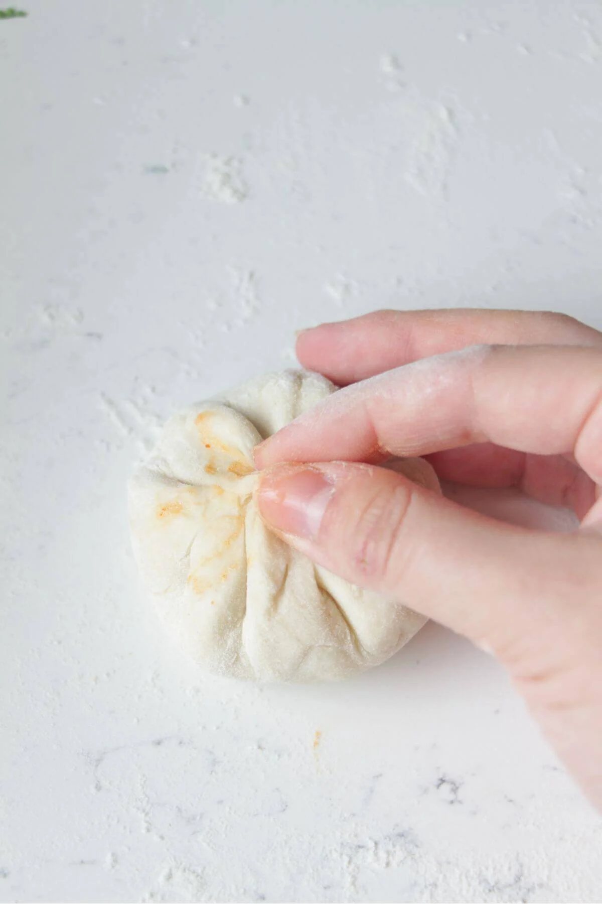 Fingers sealing the top of pizza pocket dough, to enclose the cheesy filling.