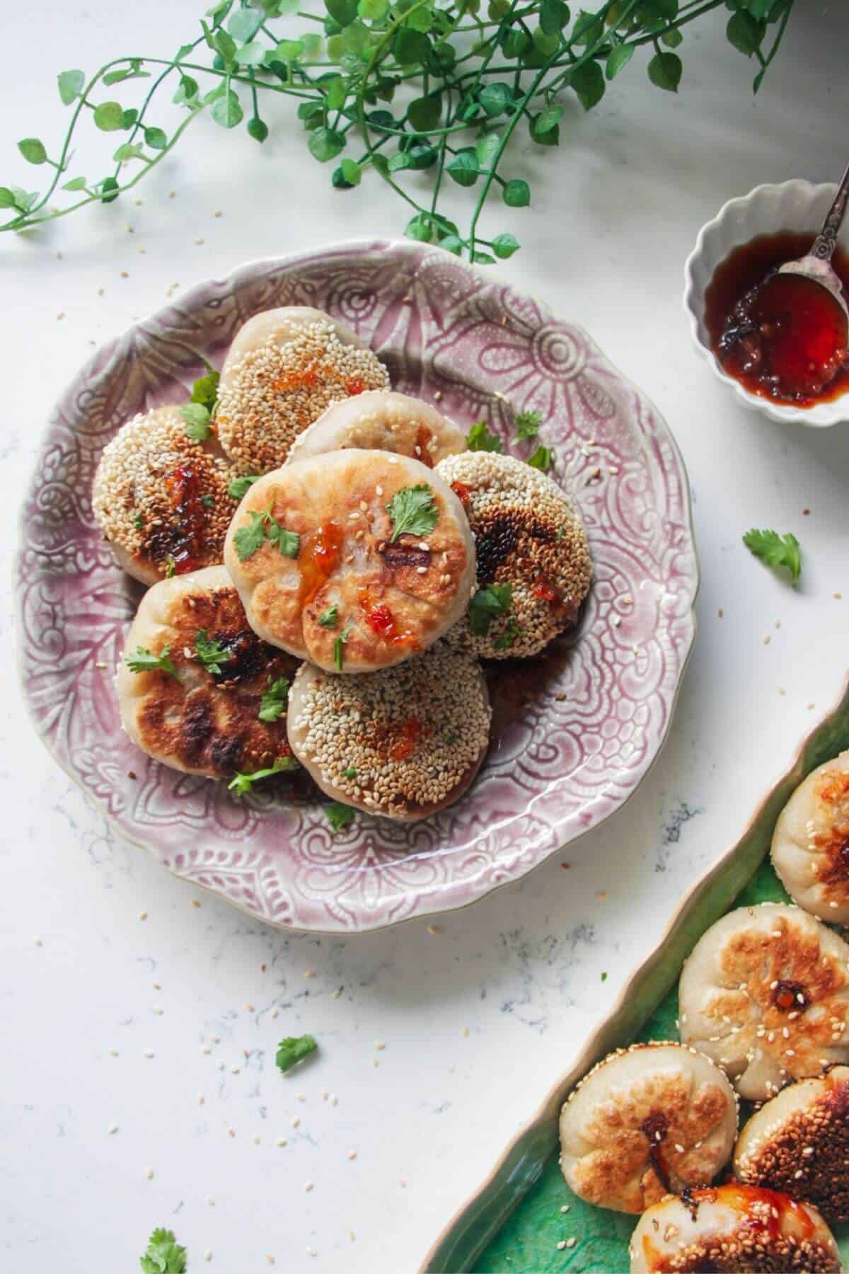 Pan-fried gochujang pizza pockets piled on a small pink plate with more pizza pockets on the side on a green plate.