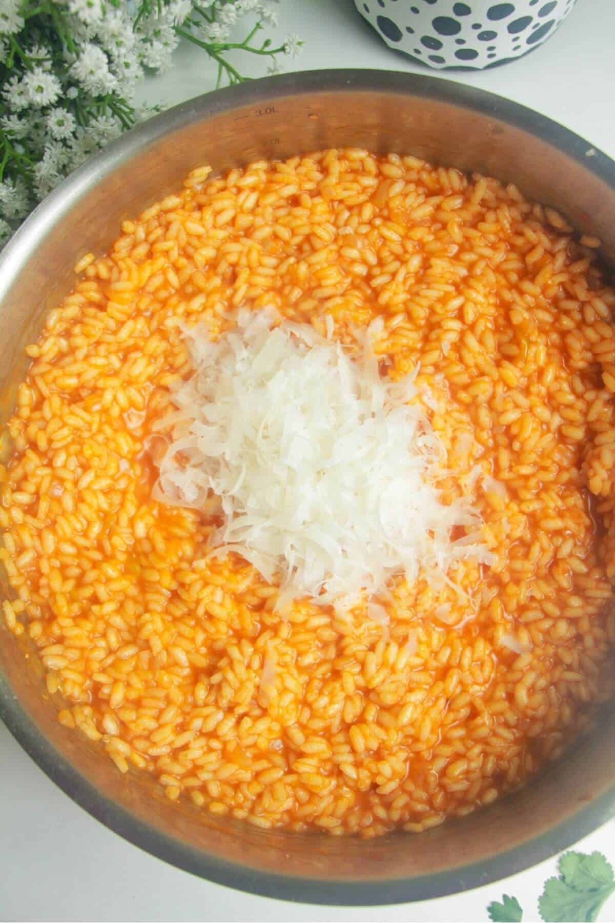 Grated parmesan on top of cooked gochujang risotto in a pan.