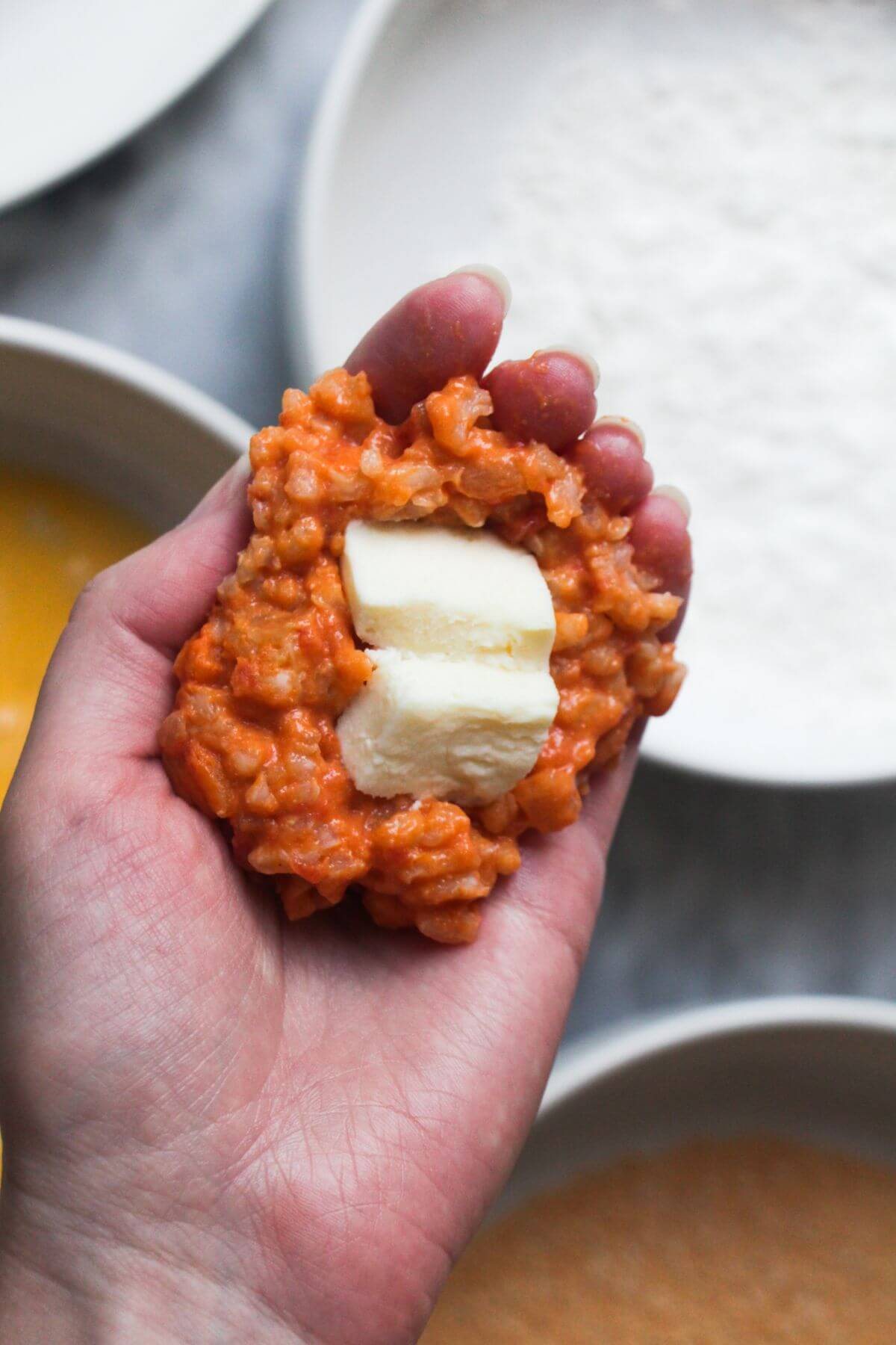 Mozzarella pieces in risotto in a hand, about to be formed into arancini.