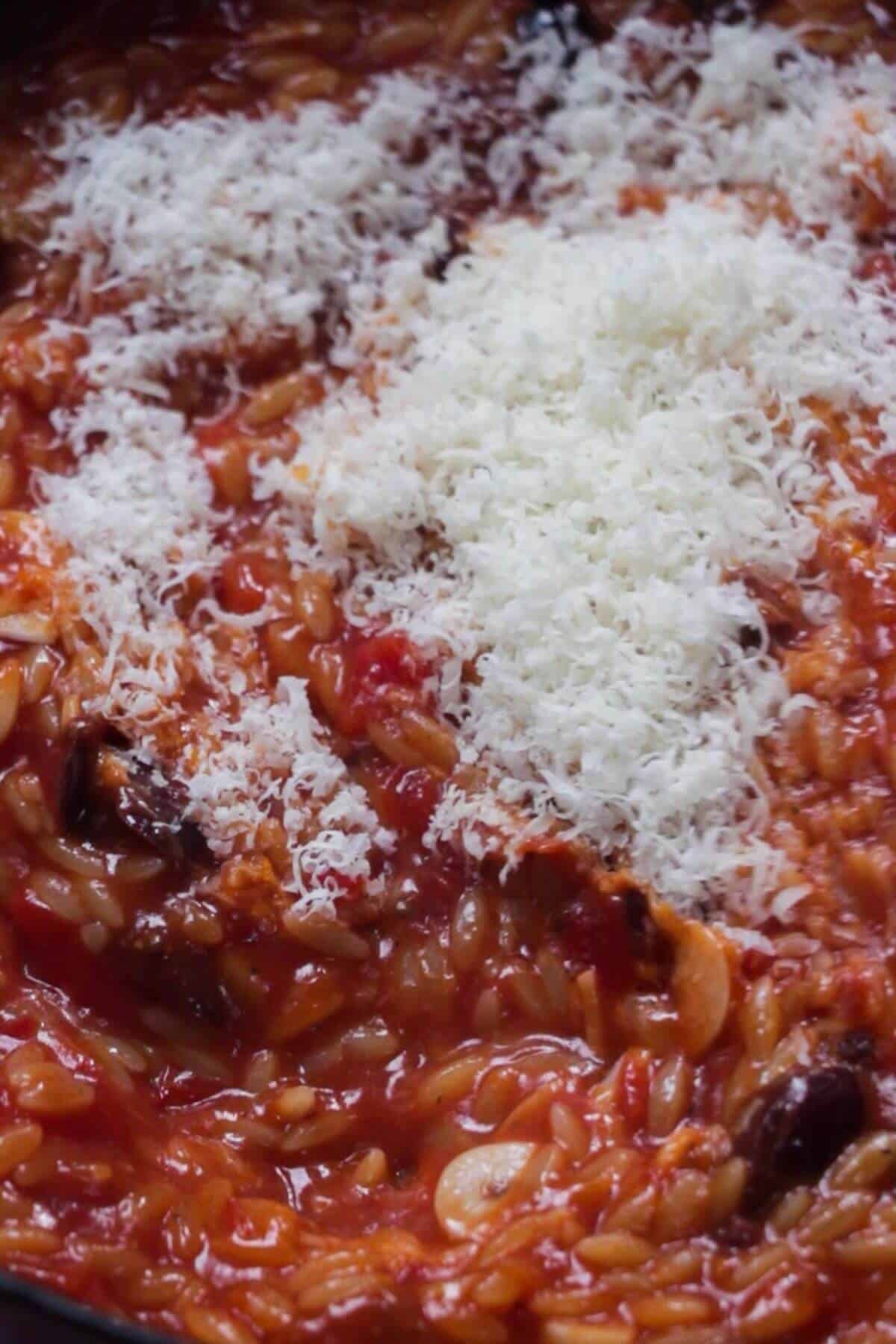 Close up of grated parmesan added to tomato orzotto.