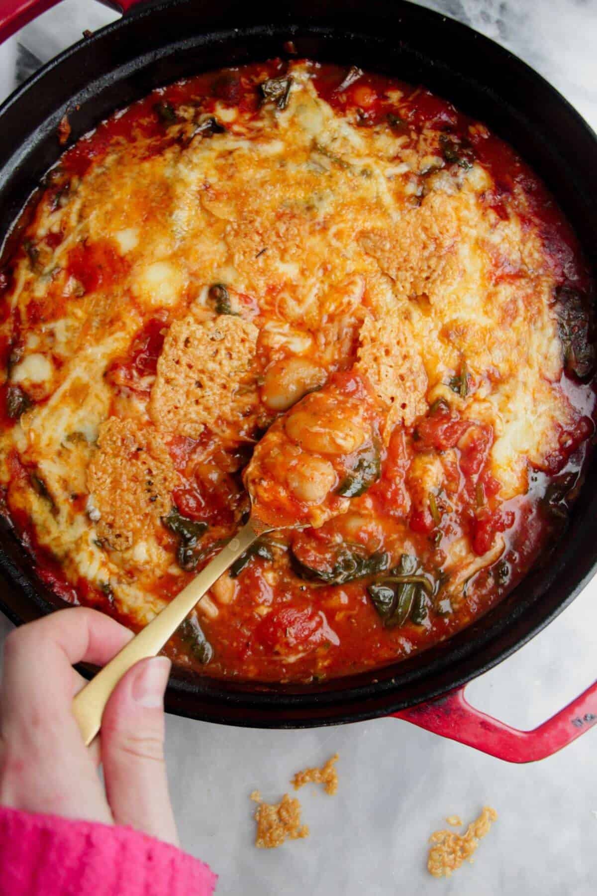 Hand holding a spoon, scooping up cheesy baked white beans.