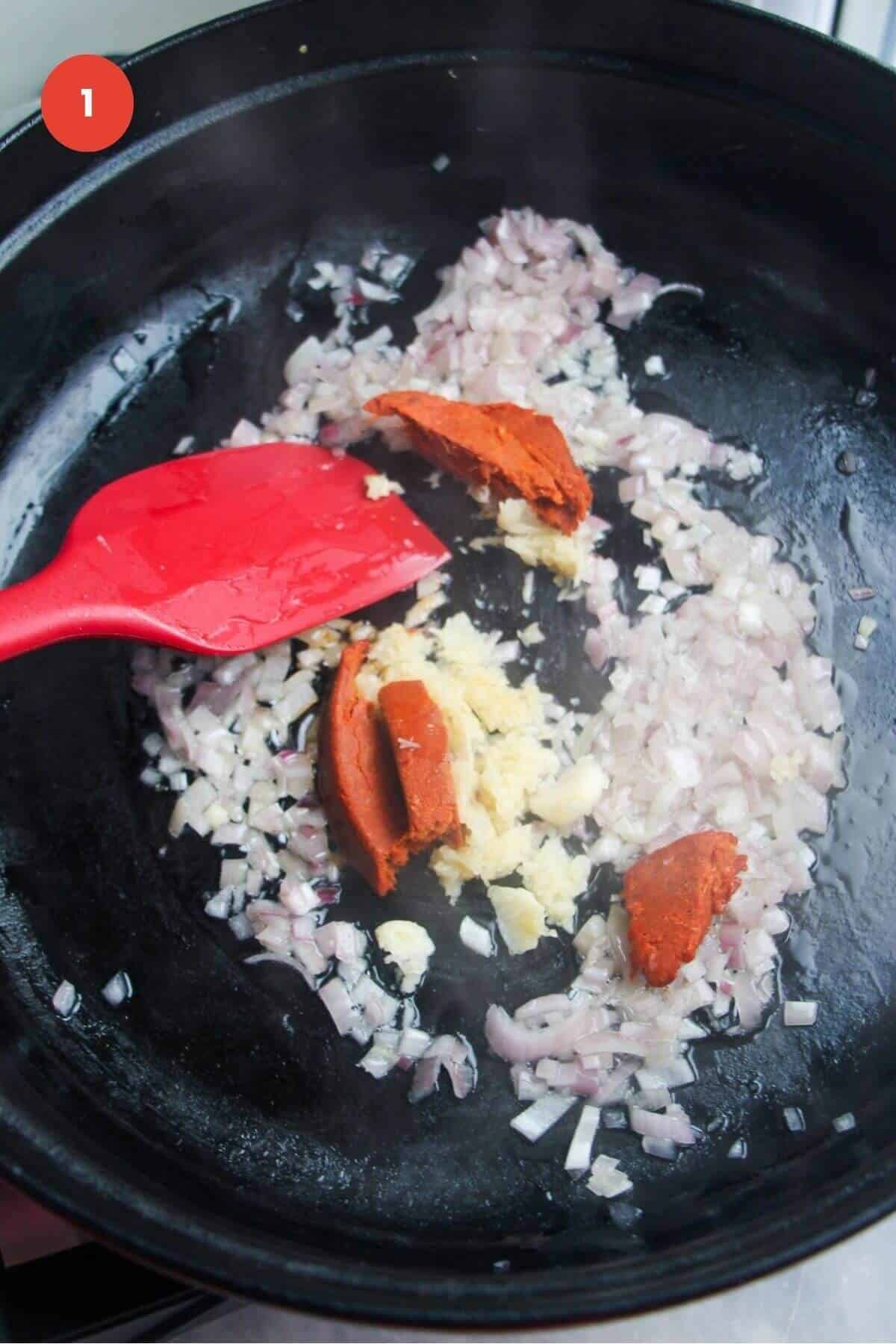 Spatula stirring diced onion and nduja in a large pan.