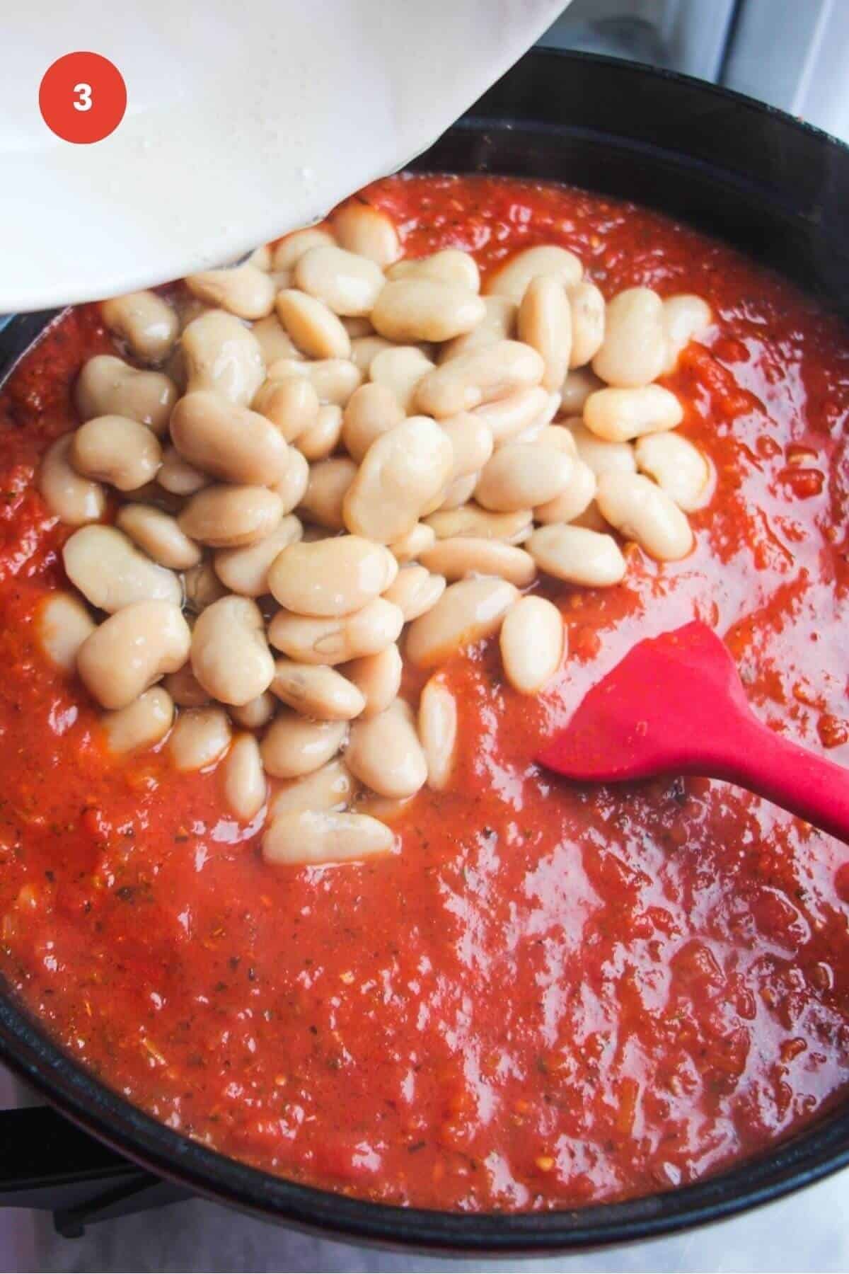 White beans added to tomato sauce in a large pan.
