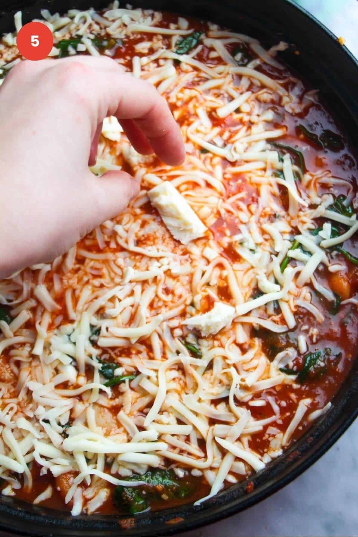 Cheese being added to the top of a white bean tomato bake.