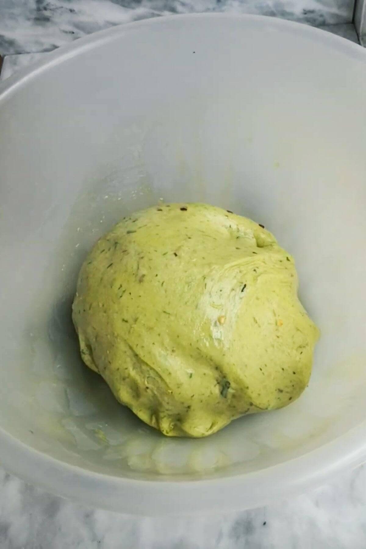 Wild garlic hot cross bun dough after kneading in a large clear bowl.