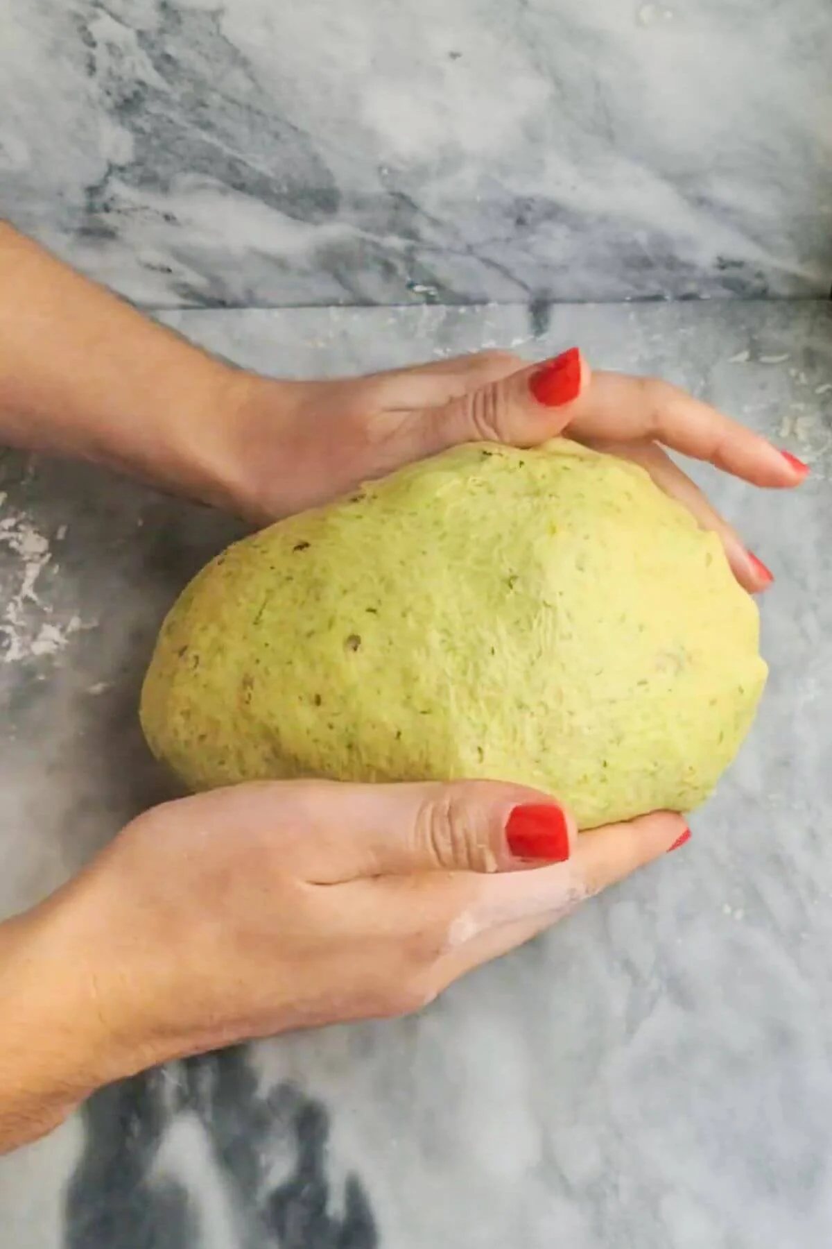 Hands forming a large dough ball on a grey marble background.