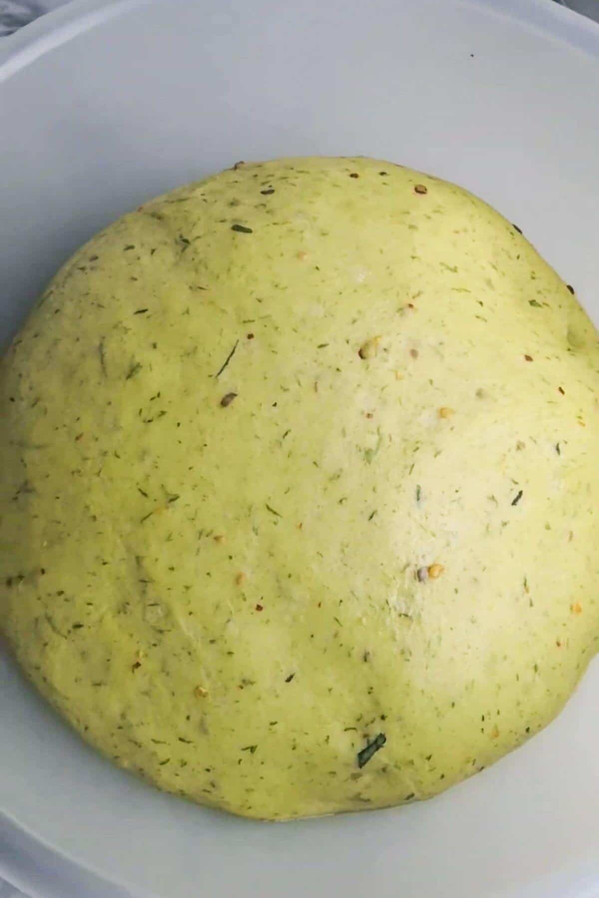 Risen, puffy wild garlic hot cross bun dough in a clear mixing bowl.