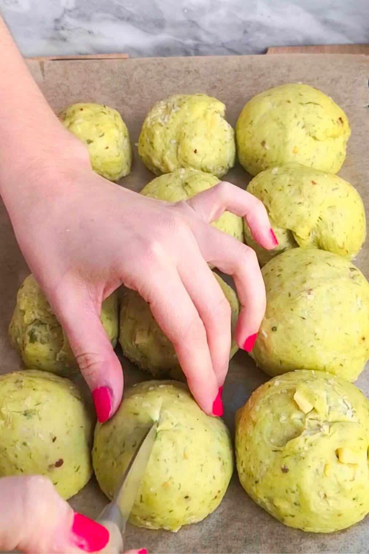 Knife slashing crosses into the top of wild garlic hot cross bun dough balls.