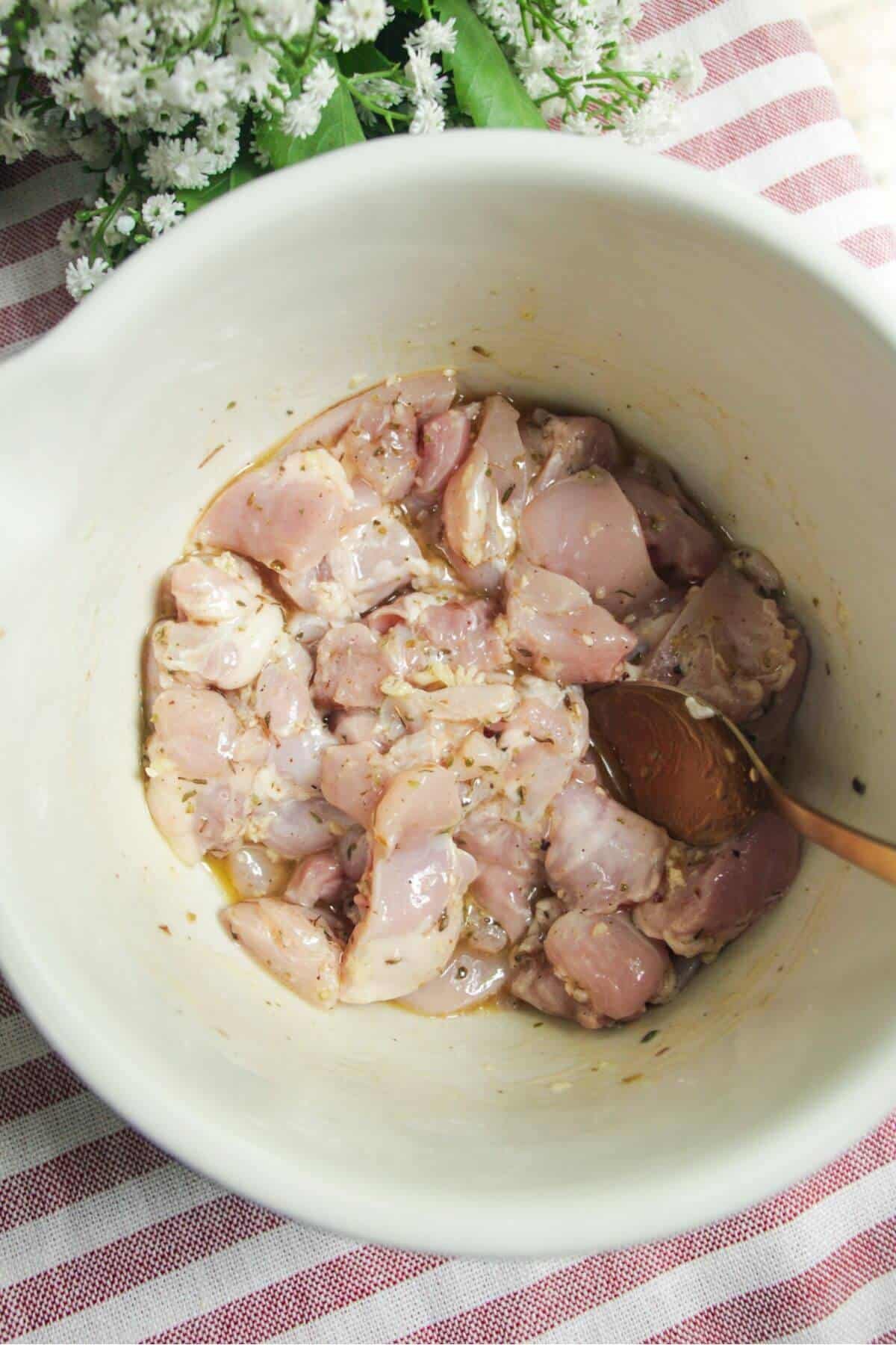 Diced chicken in a bowl with lemon juice, dried herbs and olive oil.