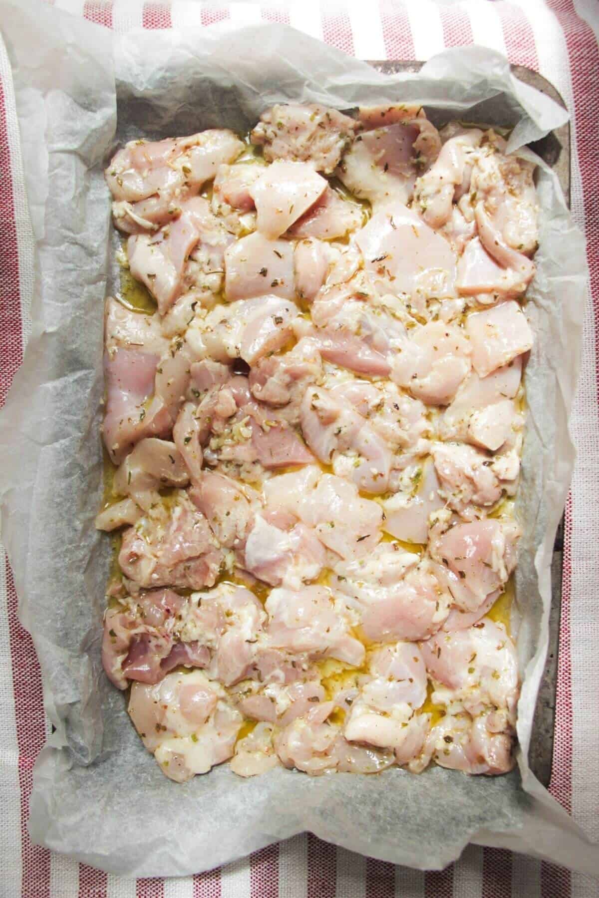 Marinated diced chicken laid out on a lined oven tray.