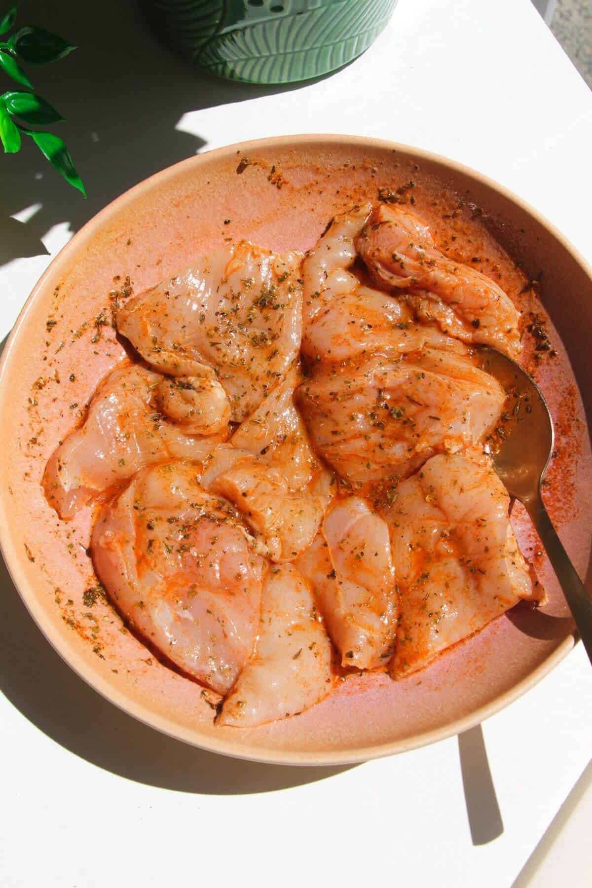 Chicken breast pieces tossed with seasoning in pink bowl.
