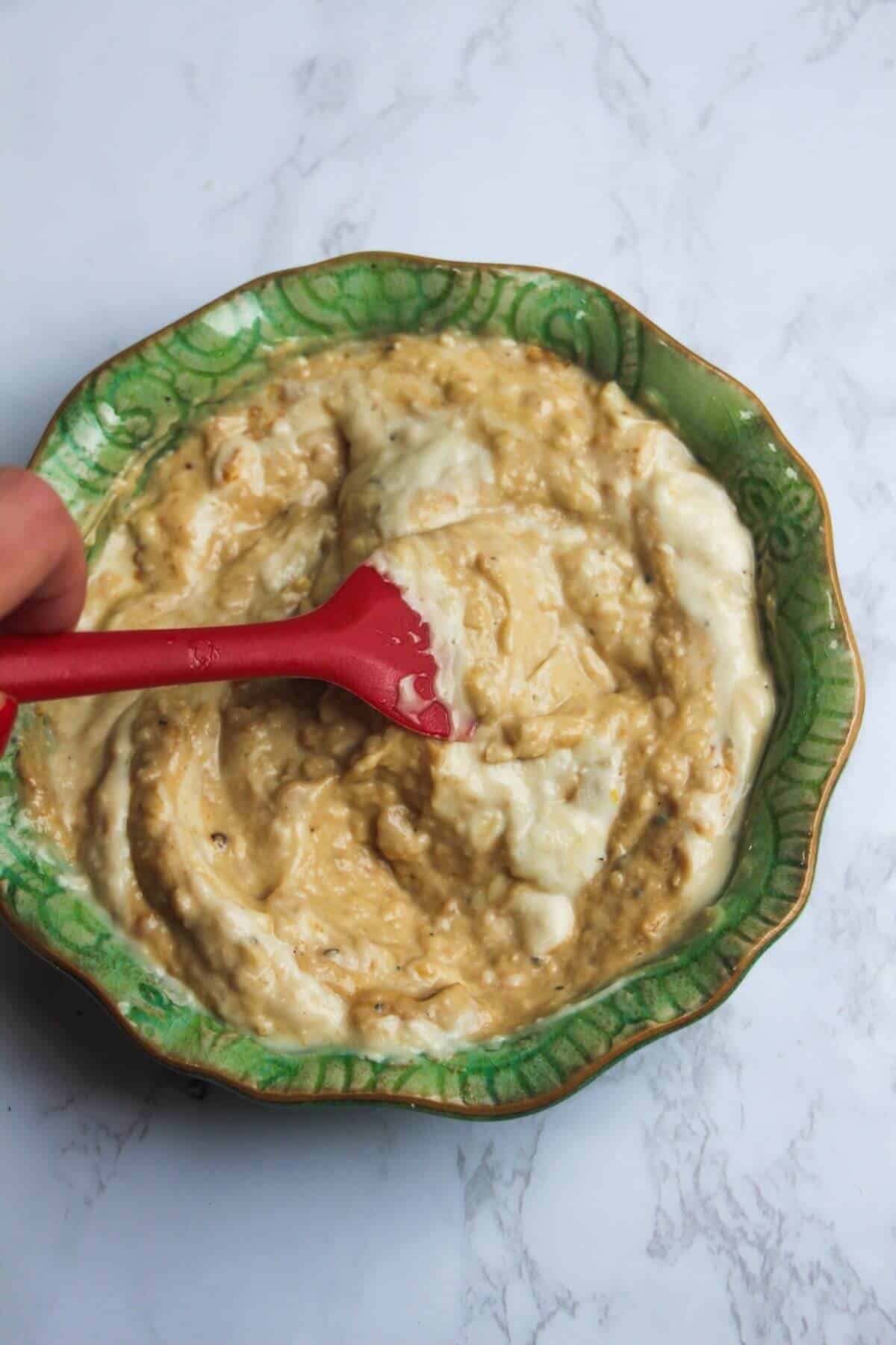 A red spatula mixing Caesar dressing in a small green bowl.