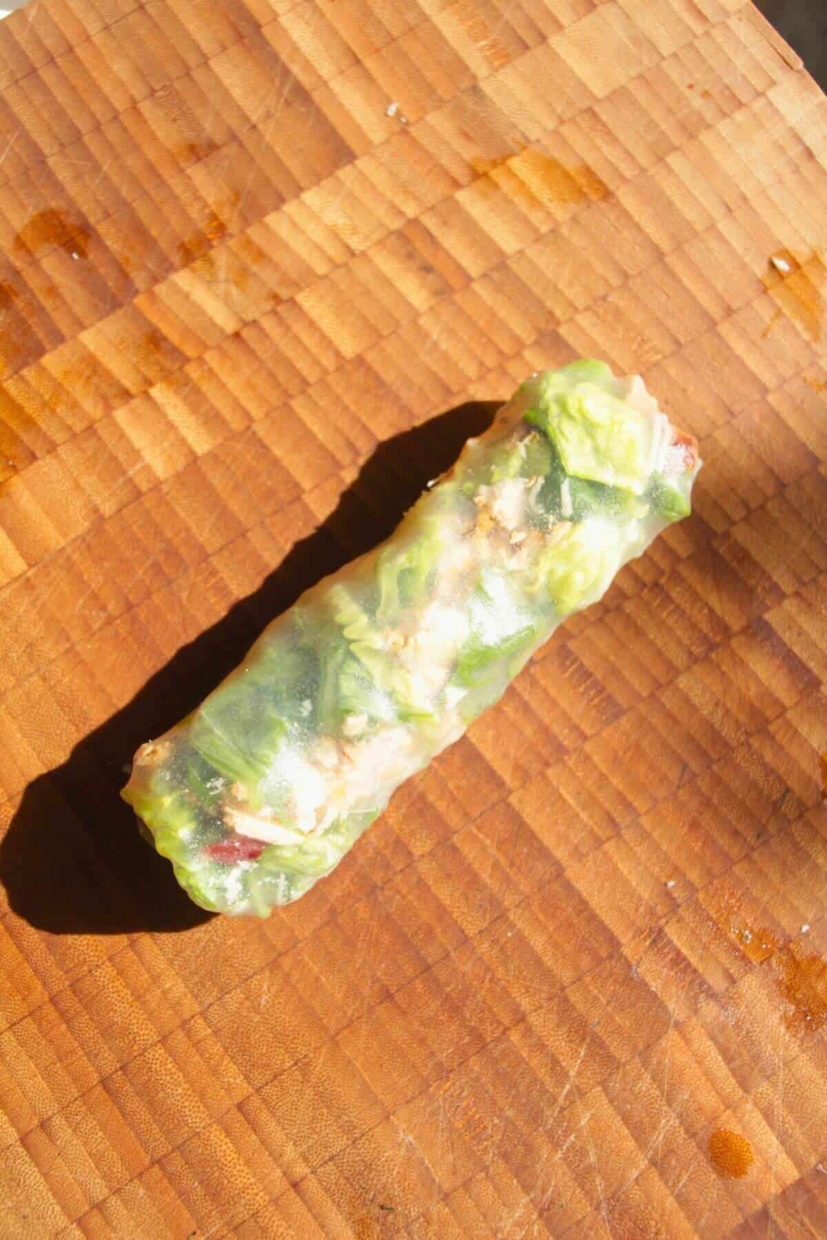 Chicken Caesar rice paper roll on a wooden board.