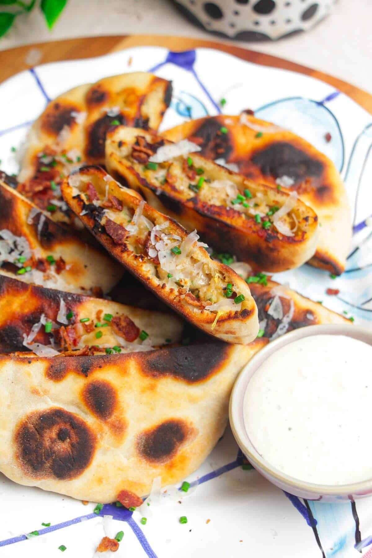 A pile of Caesar stuffed flatbreads on a platter with Caesar dip on the side.