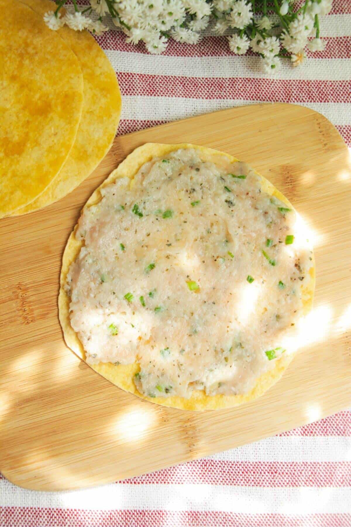 Ground chicken pressed onto a mini tortilla on a wooden board.