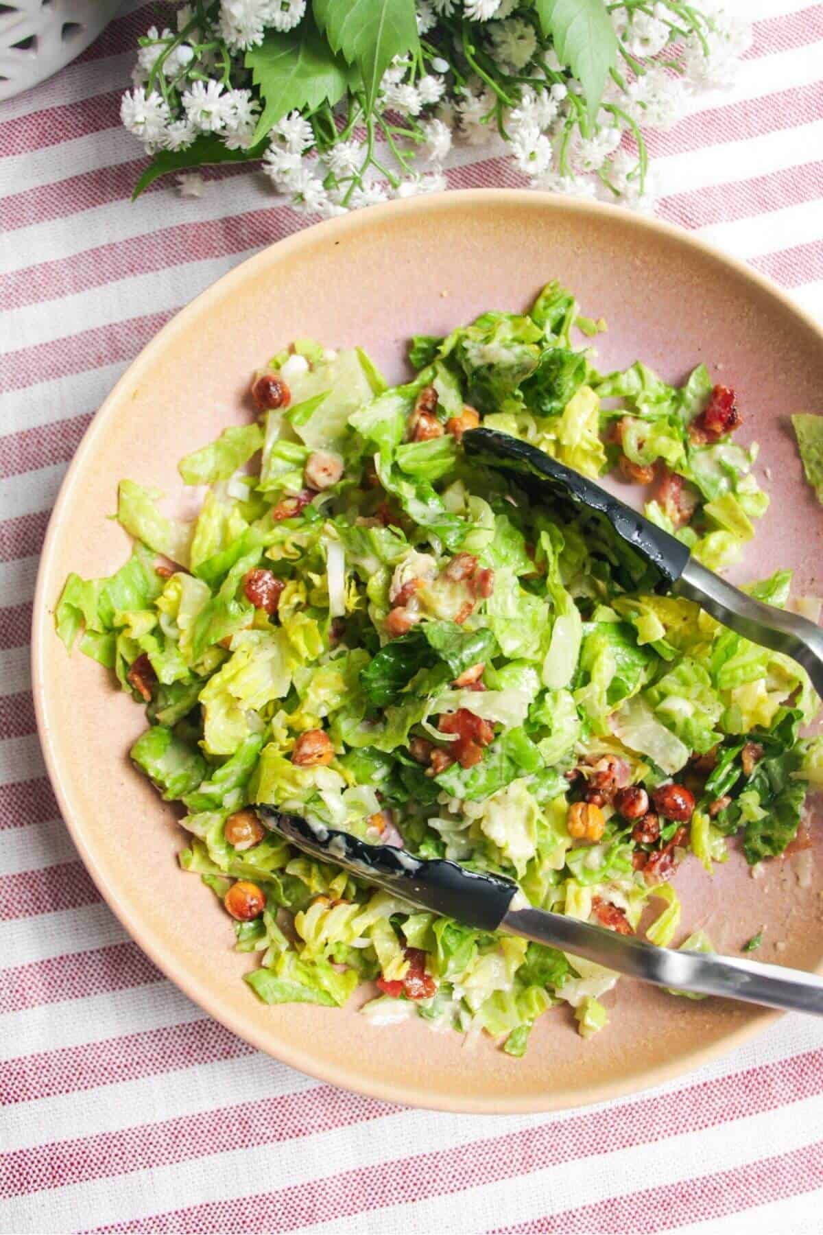 Salad mixed with tongs in a pink bowl.