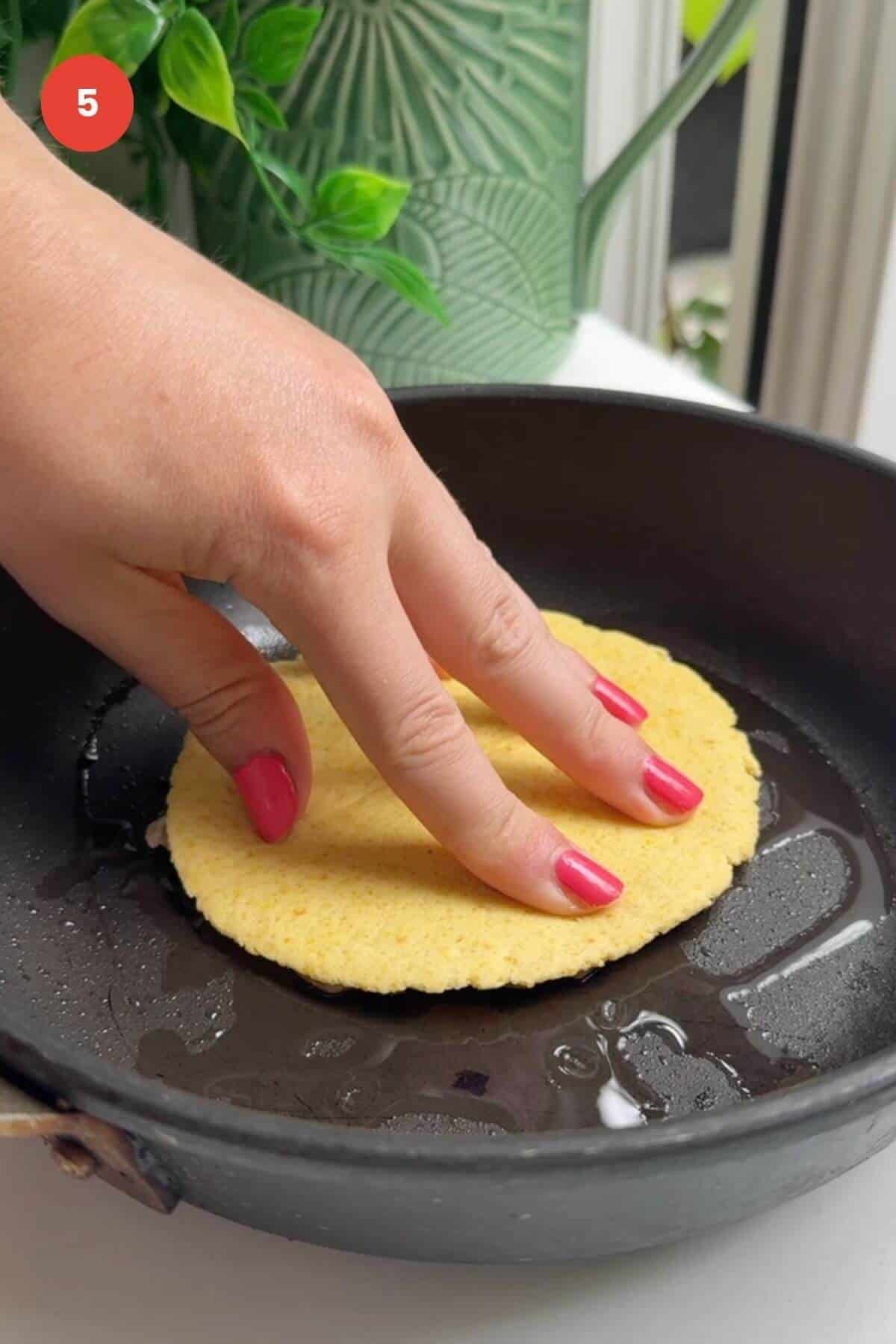 Hand pressing chicken gyros taco into pan.