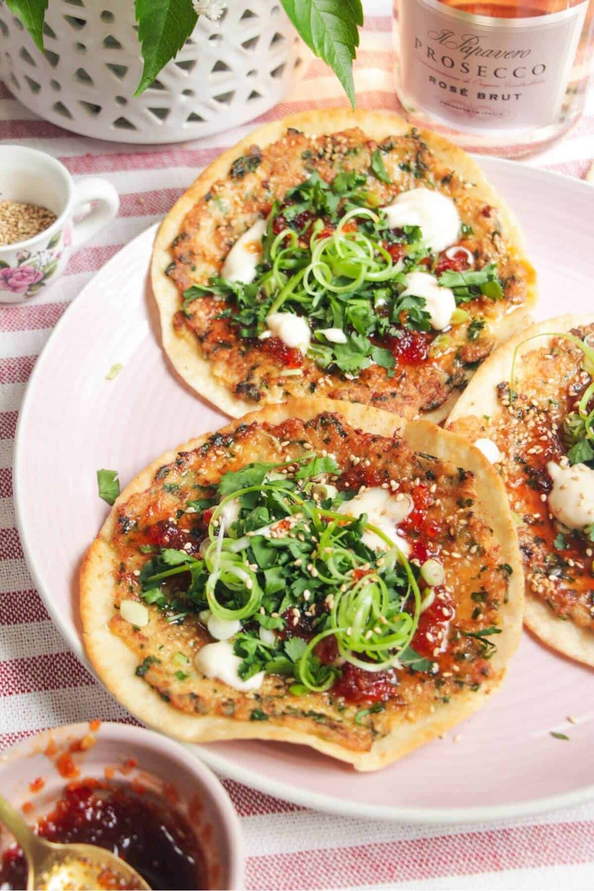 Three prawn toast tacos topped with herbs and aioli on a pink plate.